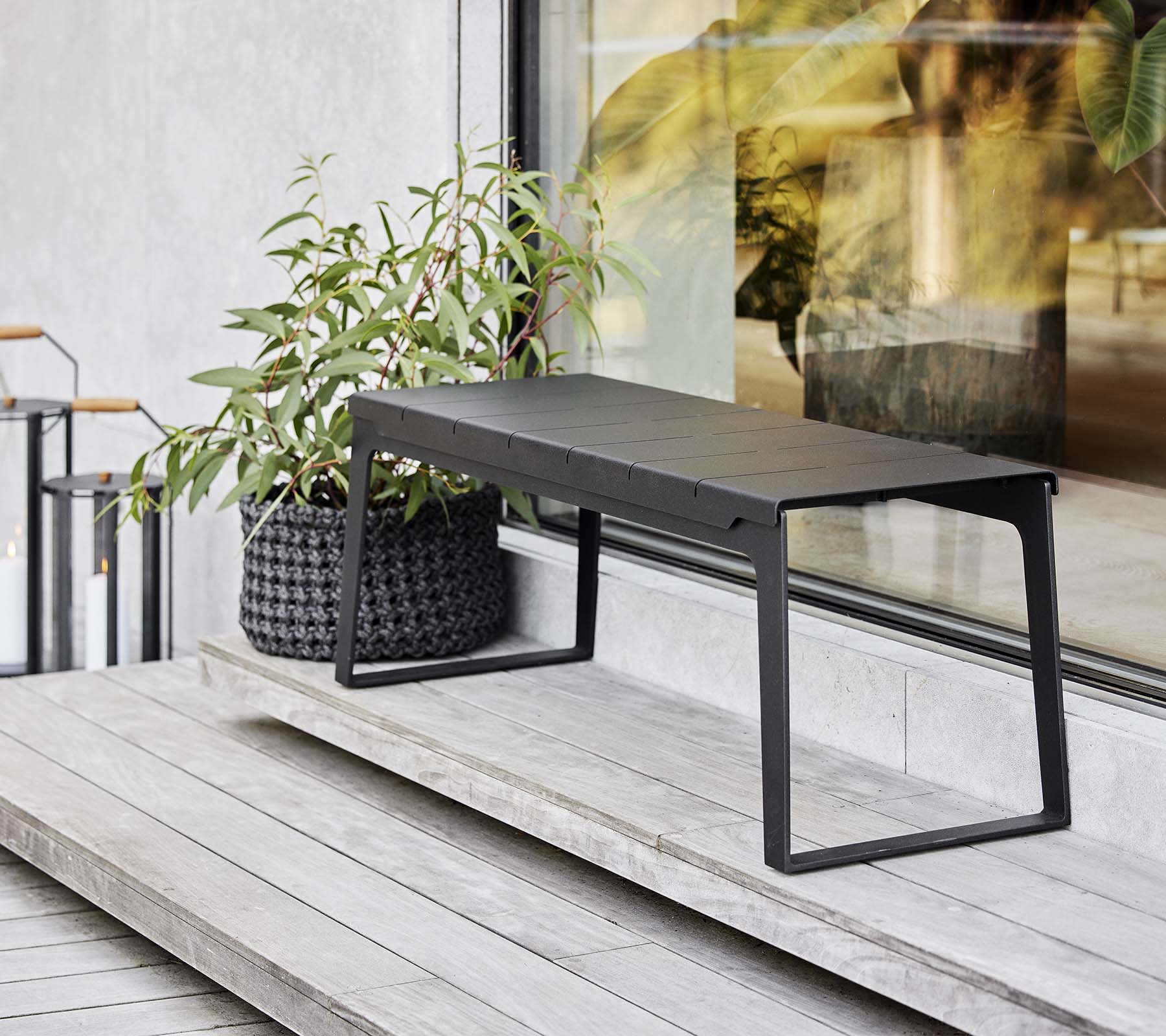 Un banc noir élégant positionné à côté d'un jardinière avec de la verdure, mettant en valeur des éléments de design modernes et une esthétique minimaliste.