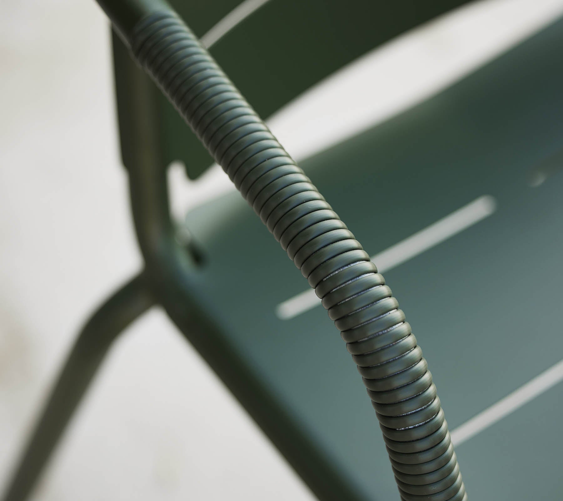 Gros plan d'une chaise Copenhagen verte, mettant en avant son accoudoir courbé et son design épuré avec des lattes subtiles sur le siège.