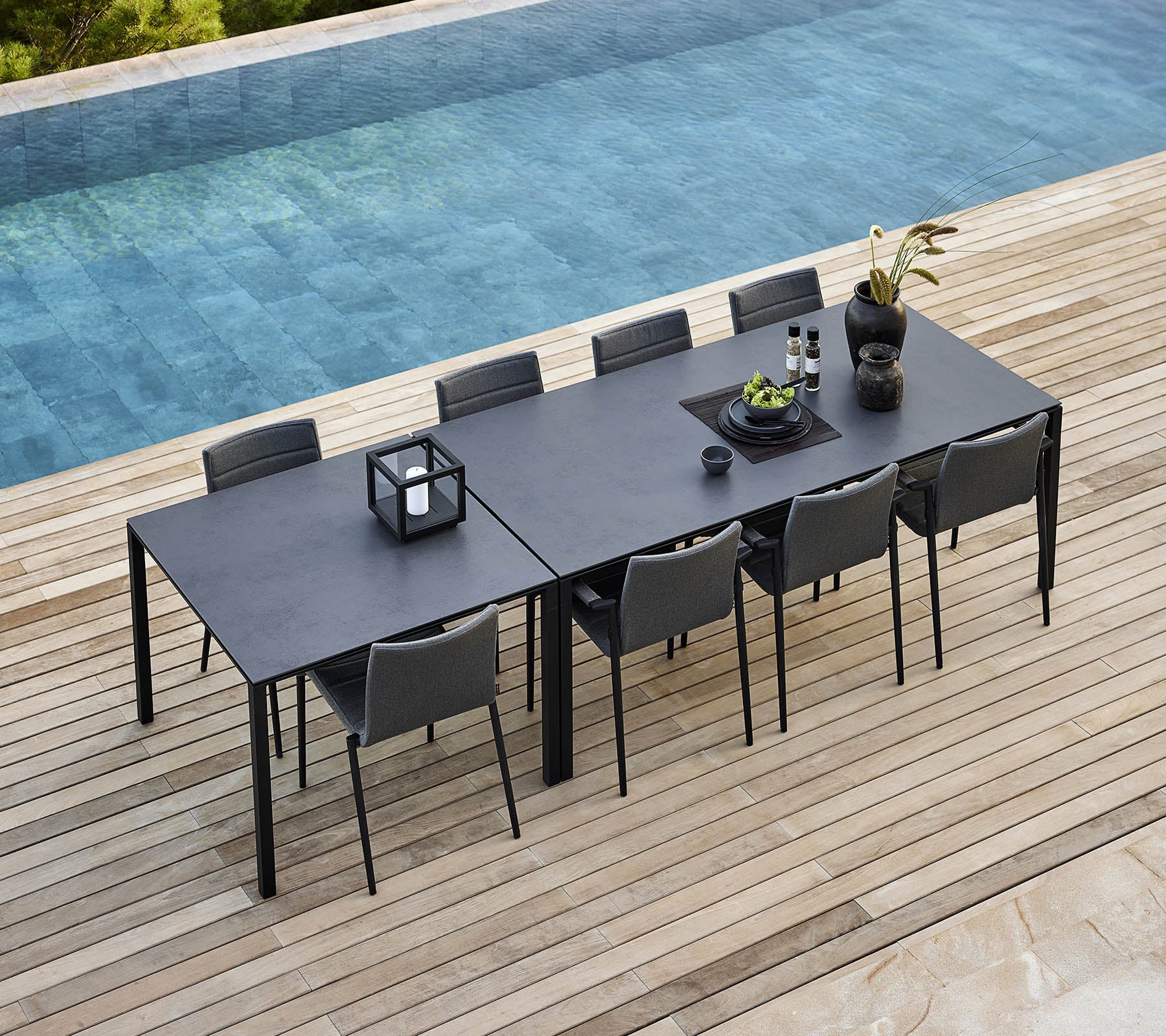 Un ensemble de salle à manger élégant avec une table épurée et des chaises modernes, décoré de plantes et d'accessoires près d'une piscine tranquille.