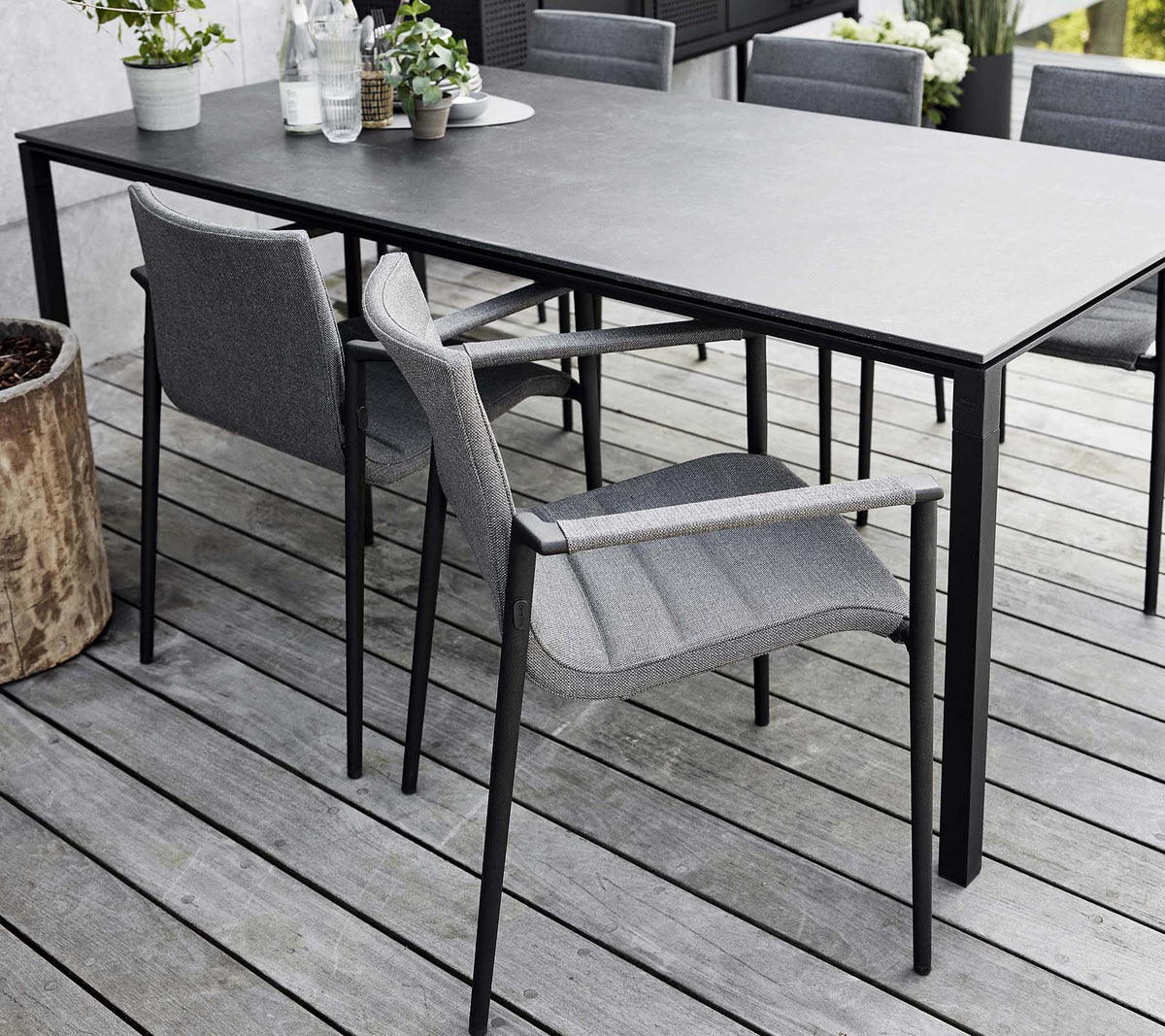 Mise en place élégante avec une table sleek et des chaises modernes gris core, entourée d'éléments naturels et de verdure.