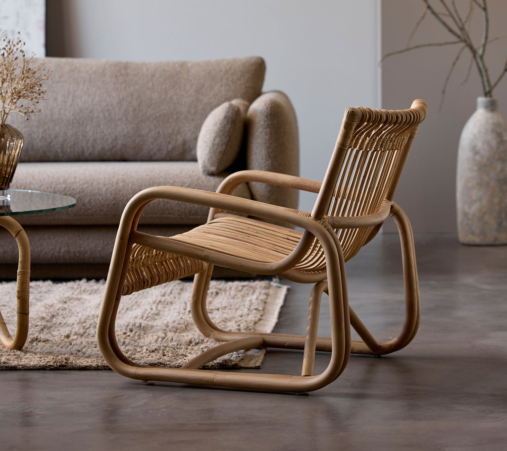 Chaise en rotin à côté d'un canapé beige et d'une table en verre dans un cadre de salon moderne.