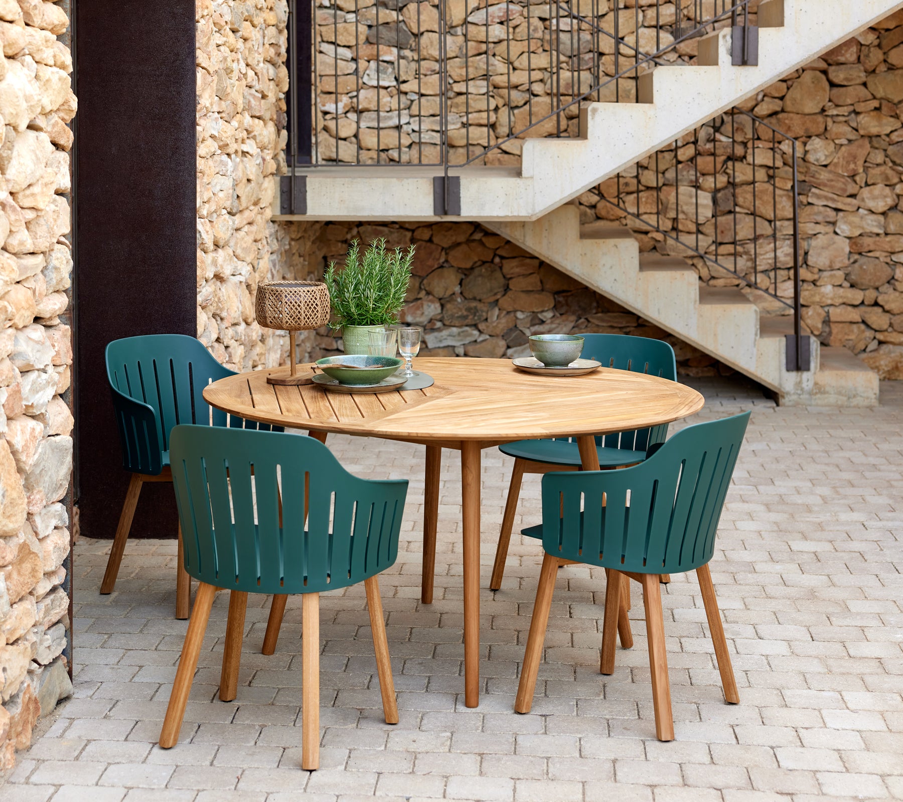 Une table ronde en bois entourée de quatre chaises vertes à lattes, complétée par des bols décoratifs et une petite plante.