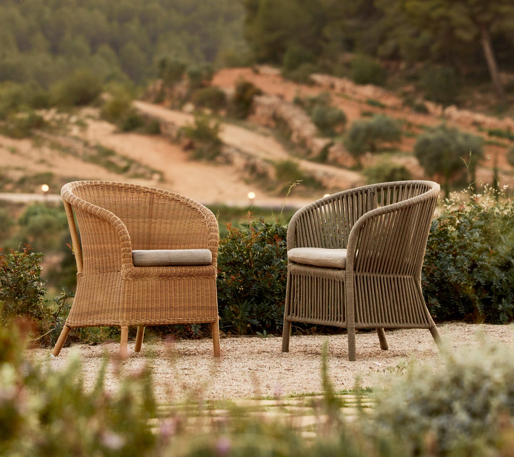 Deux chaises Derby élégantes en couleurs contrastées, placées parmi la verdure avec un décor pittoresque.