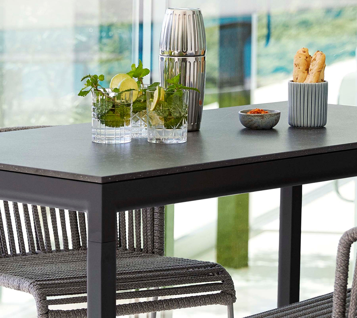 Une table moderne garnie de plantes dans des vases en verre, un contenant décoratif et un plat de collations, entourée de chaises élégantes.