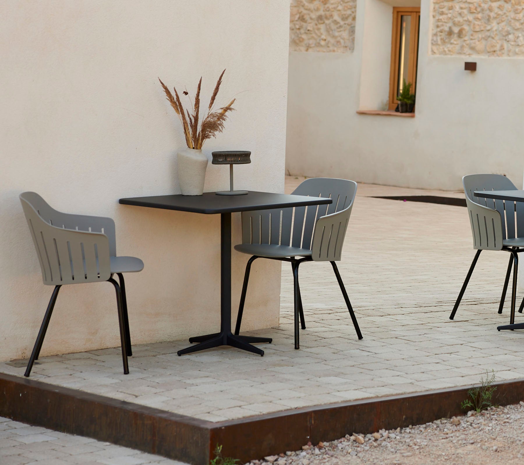 Une table de café moderne avec deux chaises grises élégantes, accompagnée d'un vase décoratif, sur un fond simple.