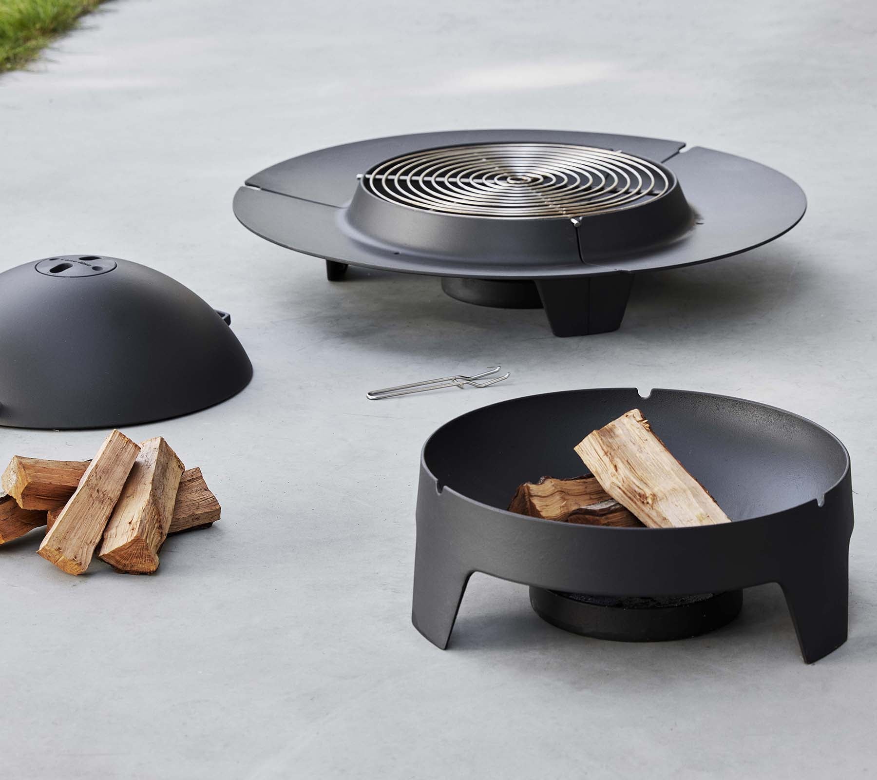 Un foyer noir élégant avec une grille de cuisson, une housse de protection et une base, accompagné de bûches empilées.