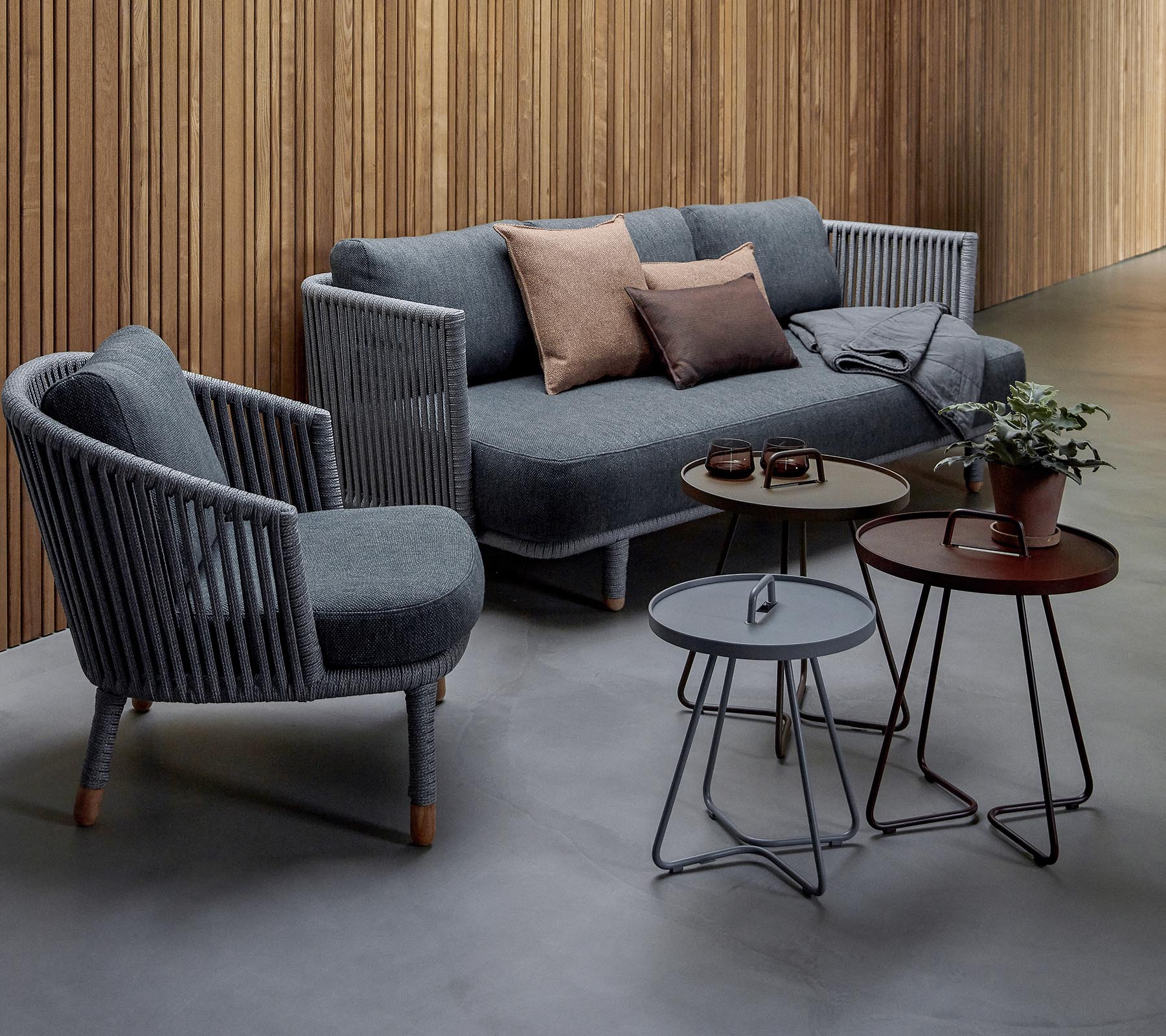 Aménagement de sièges élégant avec un canapé gris avec des coussins et deux fauteuils d'accent, accompagné de trois tables modernes et d'une plante en pot.