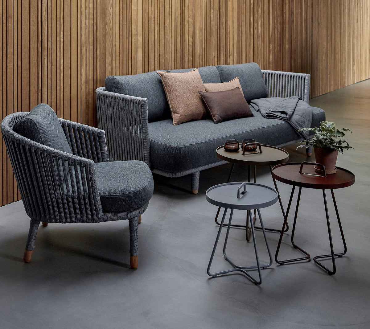 Aménagement de sièges élégant avec un canapé gris avec des coussins et deux fauteuils d'accent, accompagné de trois tables modernes et d'une plante en pot.