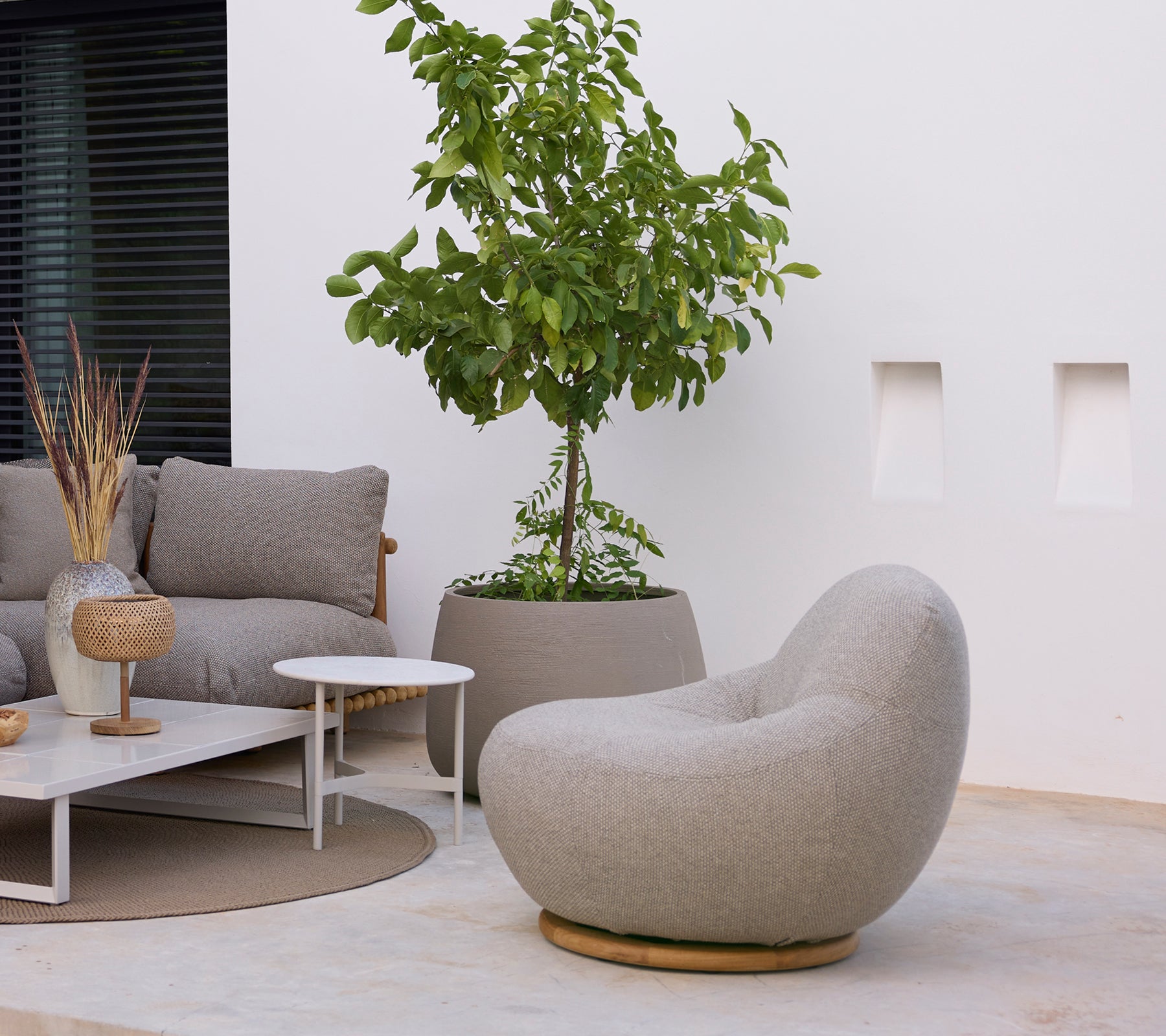 Espace salon moderne avec une chaise grise, un canapé, une table basse blanche et une plante verte.