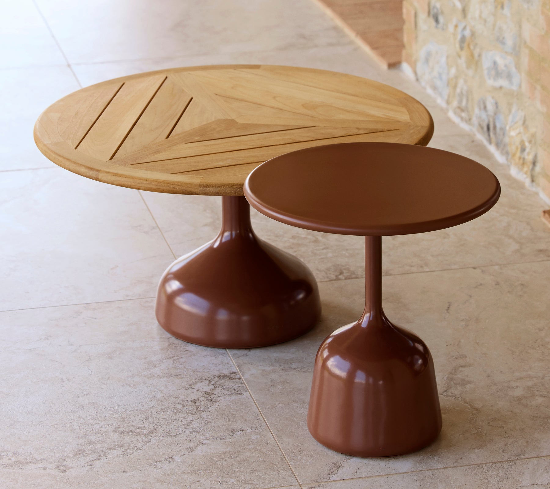 Deux tables basses, l'une avec un plateau en bois et un design géométrique, l'autre avec une finition lisse, rouge désert, partageant une esthétique moderne.