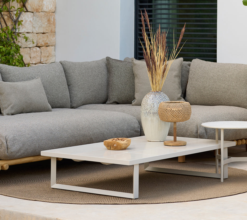 Espace lounge moderne avec un canapé gris et une table basse blanche avec décoration.