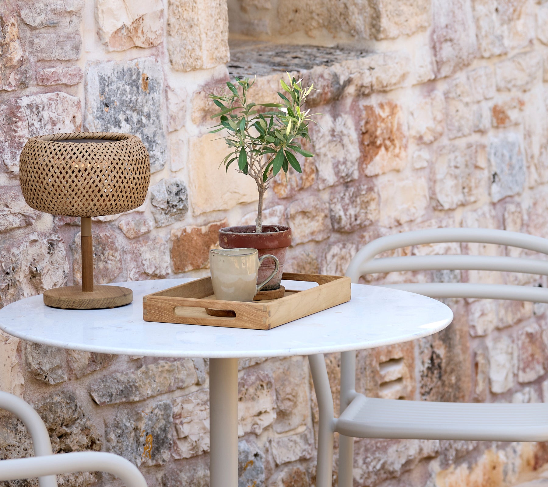 Aménagement extérieur moderne avec une table blanche, une lampe tissée, un plateau en bois et une plante en pot.