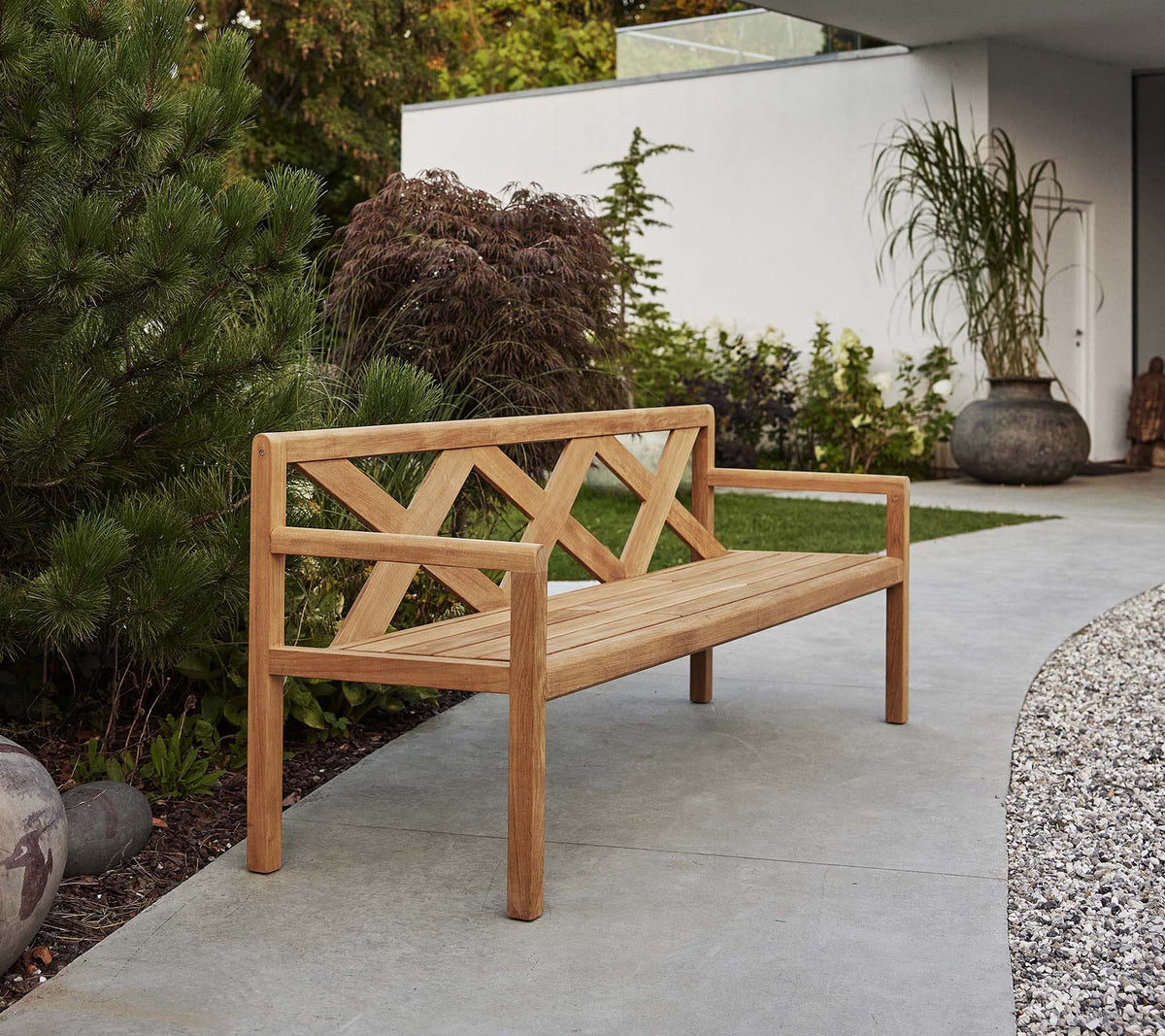 Un banc en bois élégant avec un dossier décoratif, entouré de verdure et d'éléments décoratifs, parfait pour se détendre à l'extérieur.