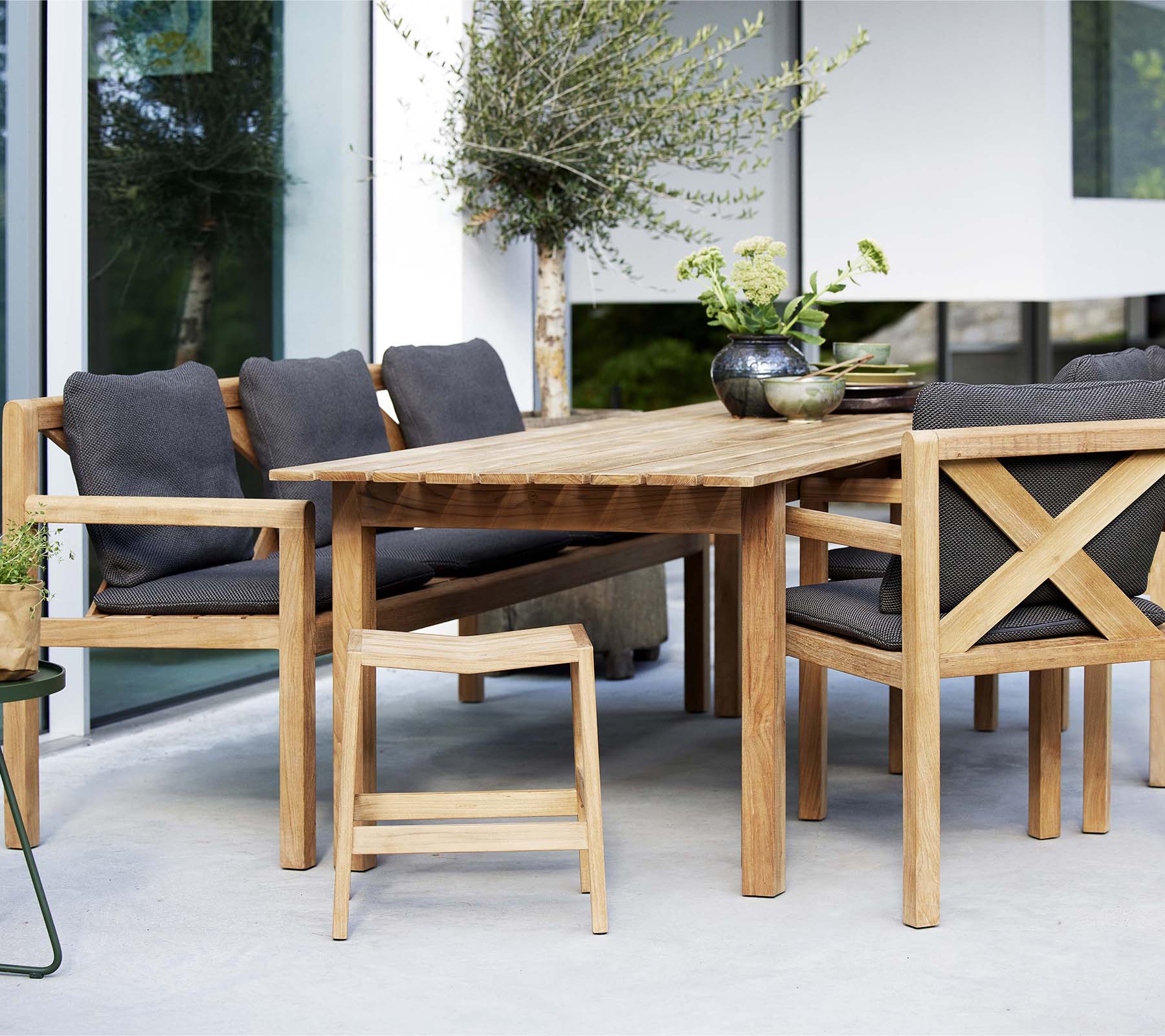 Une table en bois entourée de chaises élégantes et d'un banc, avec des coussins doux et des plantes décoratives pour un coin salon accueillant.