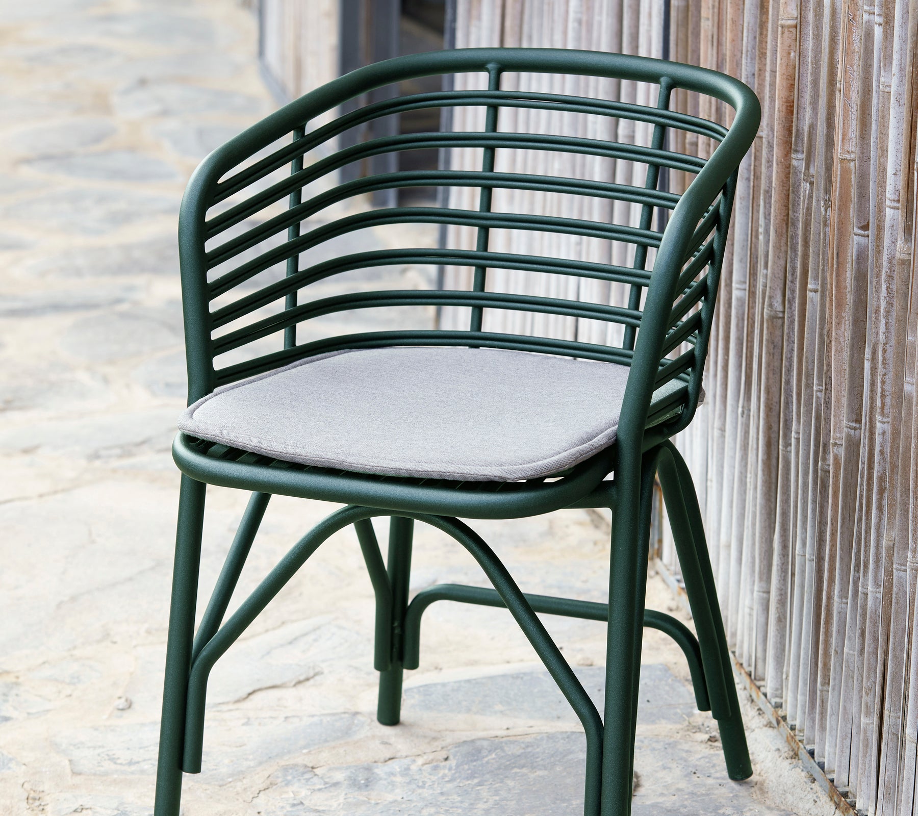 Chaise en mélange vert avec un dossier incurvé et un coussin gris doux, conçu pour le confort et le style.