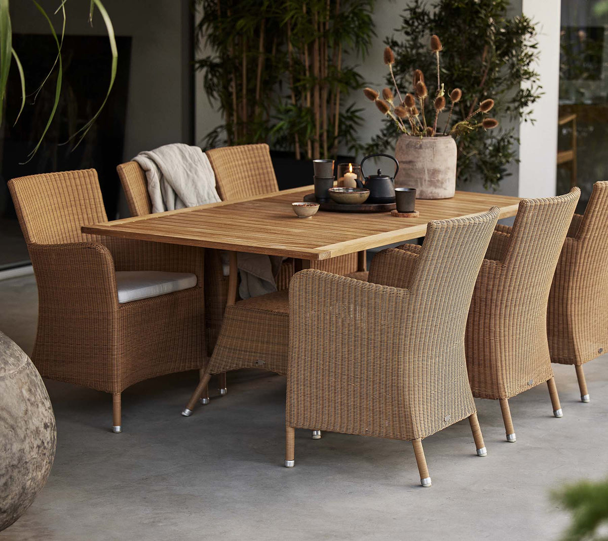 Un agencement de salle à manger avec une table en bois rustique entourée de chaises Hampsted tissées, complété par des plantes décoratives.
