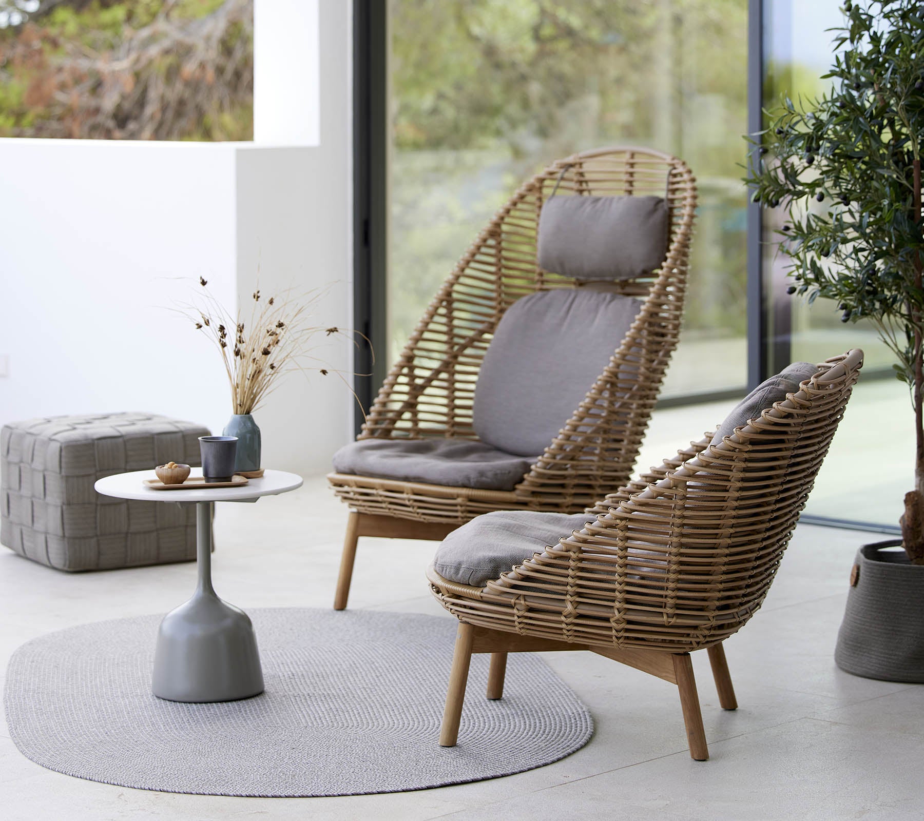 Deux chaises tissées élégantes avec des coussins, accompagnées d'une petite table ronde et d'éléments décoratifs, posées sur un tapis circulaire.