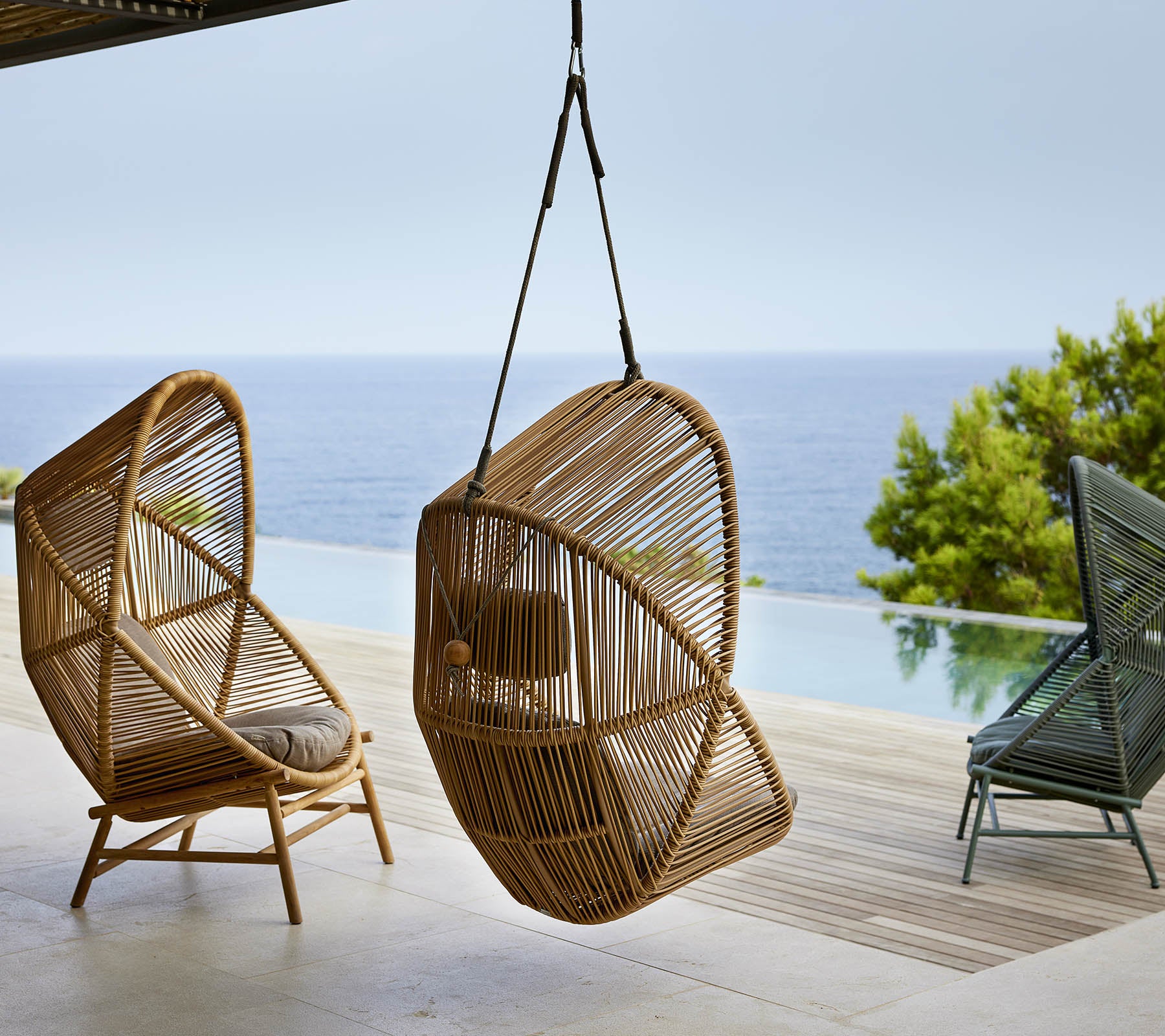 Une paire de chaises suspendues élégantes en matière tissée, positionnées près d'un plan d'eau serein, avec de la verdure en arrière-plan.