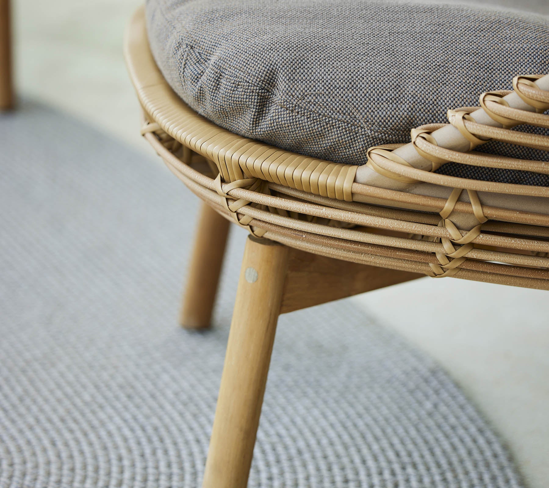 Un gros plan d'une chaise lounge élégante avec un cadre tissé et un siège rembourré, complété par un tapis texturé en dessous.