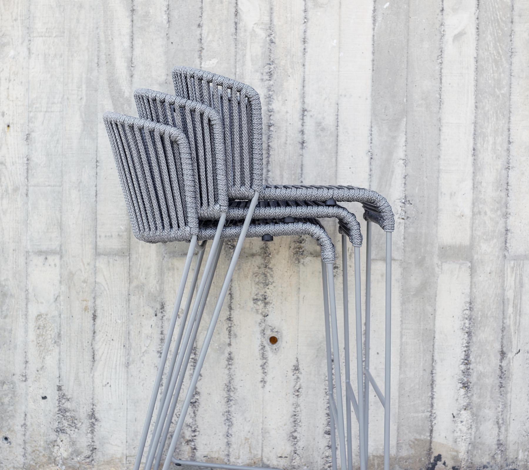 Chaises grises empilées contre un mur en béton texturé.