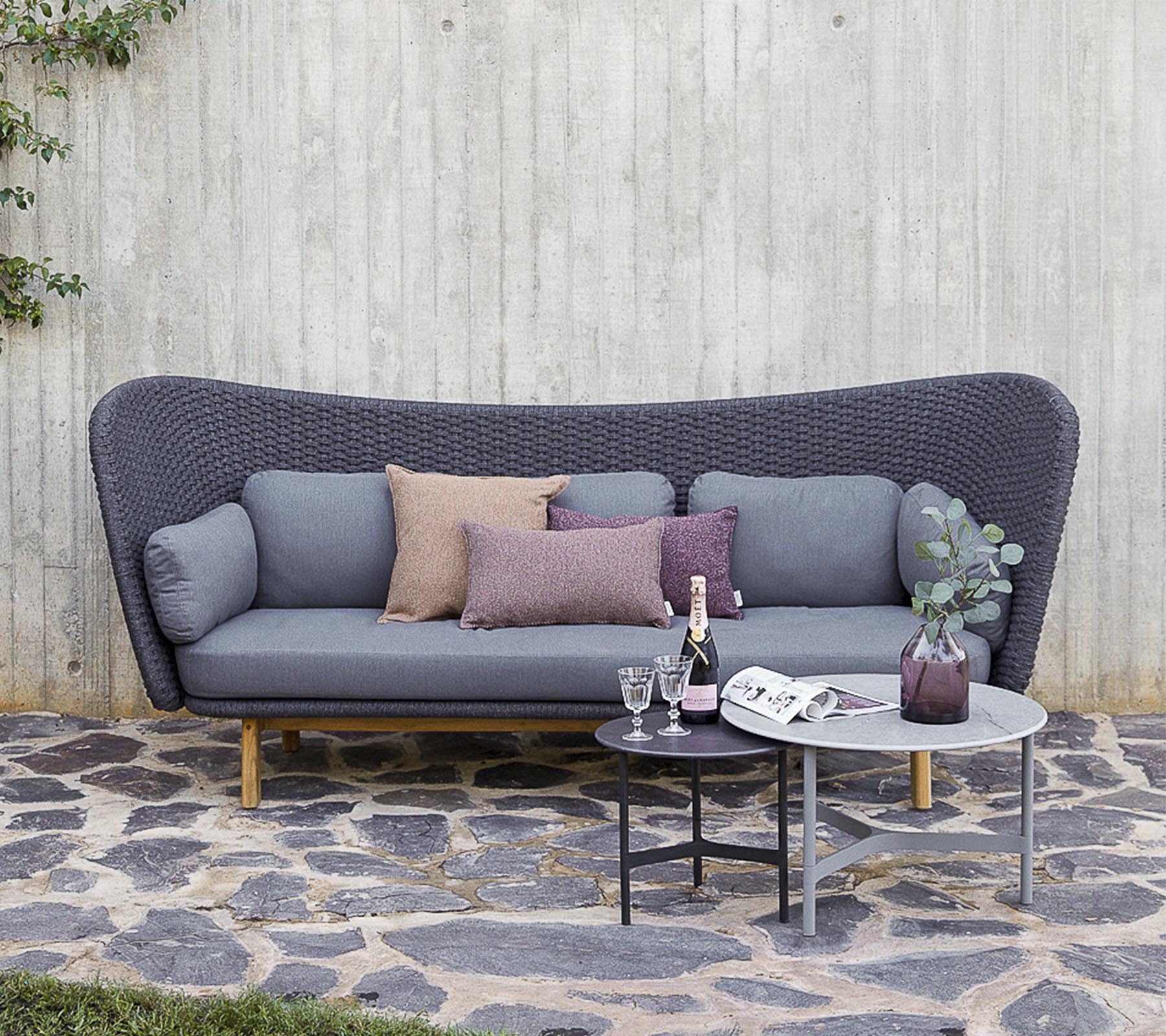 Un canapé moderne en gris avec des coussins décoratifs, accompagné d'une petite table avec des boissons et un vase, se dressant contre un mur texturé.