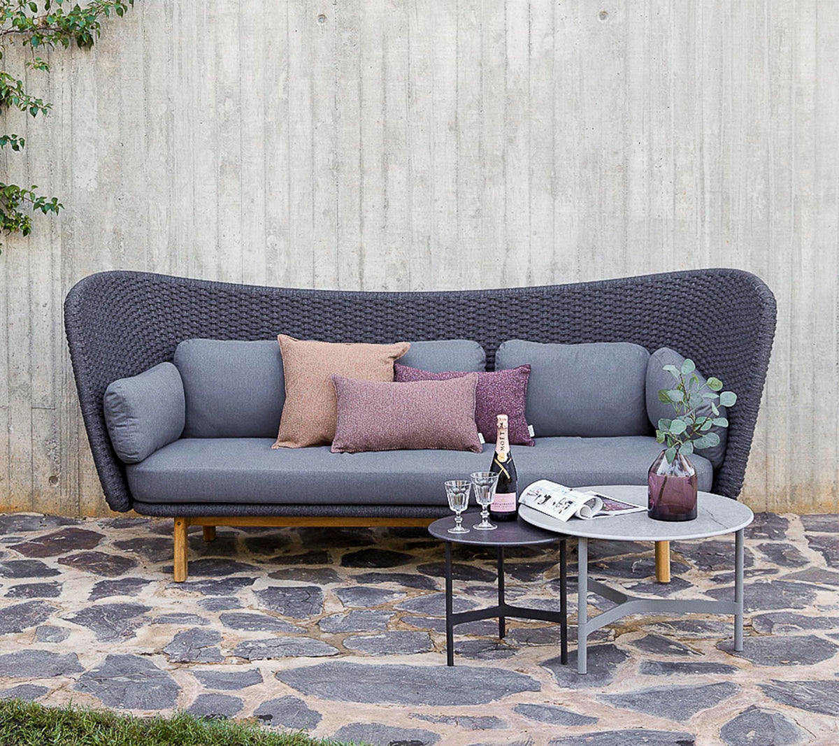 Un canapé moderne en gris avec des coussins décoratifs, accompagné d'une petite table avec des boissons et un vase, se dressant contre un mur texturé.