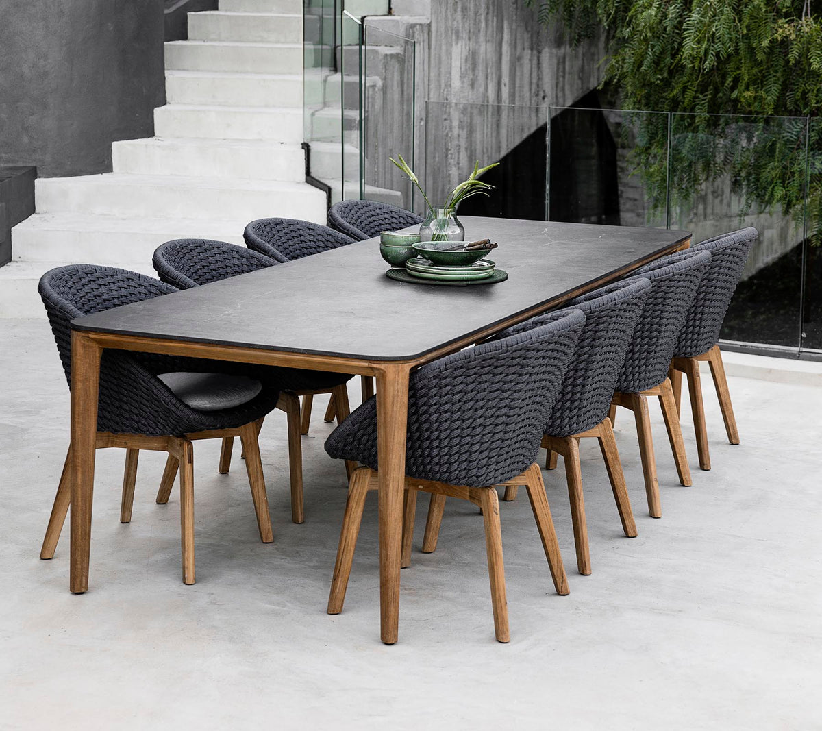 Une table moderne entourée de huit chaises élégantes, ornée de plantes décoratives sur la table dans un cadre épuré et minimaliste.