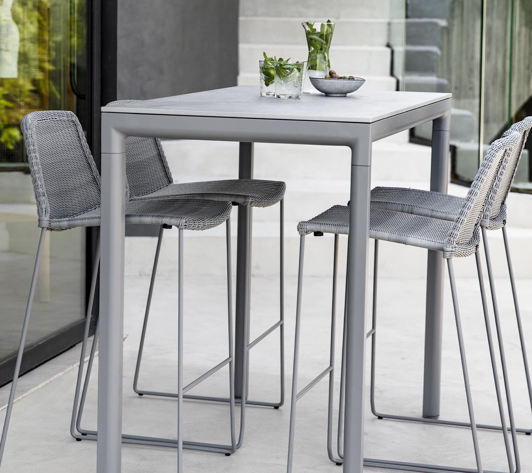 Une table grise moderne avec trois tabourets assortis, comportant des plantes décoratives et un bol sur la surface de la table.