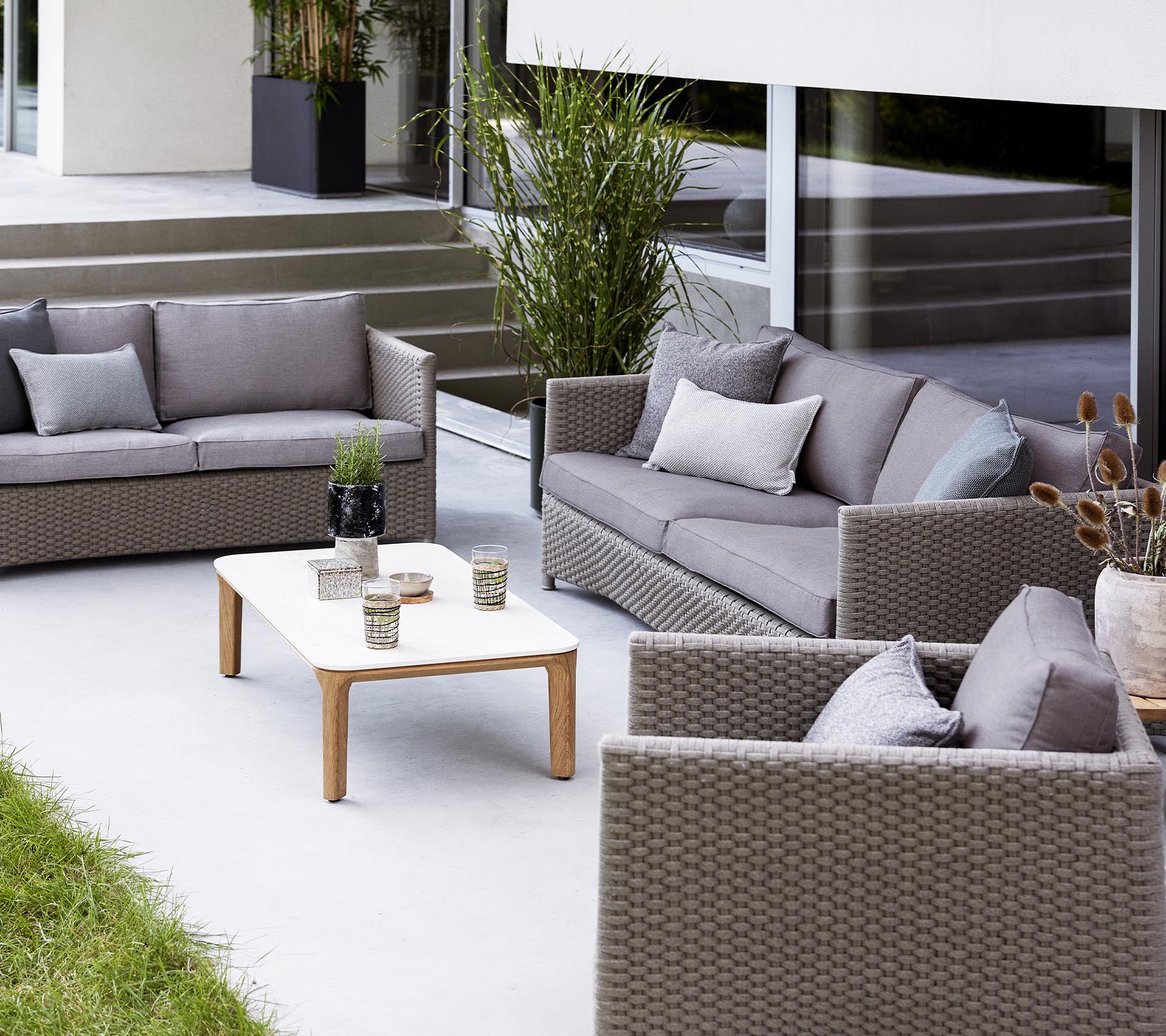 Agencement contemporain d'extérieur avec un canapé 2 places, un canapé 3 places, des fauteuils lounge et une table basse avec des objets décoratifs.