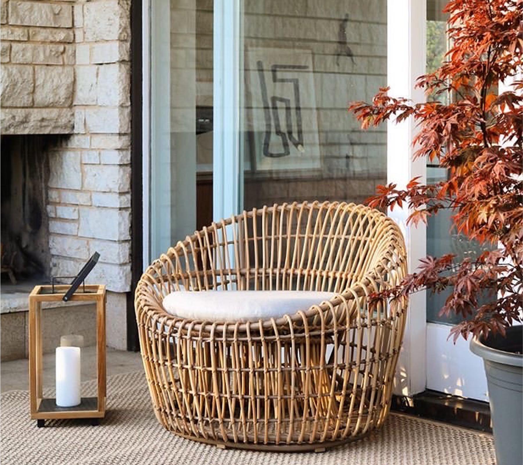 Une chaise en osier élégante avec un coussin, accompagnée d'une lanterne et d'une plante vibrante, enrichissant un espace chaleureux et accueillant.