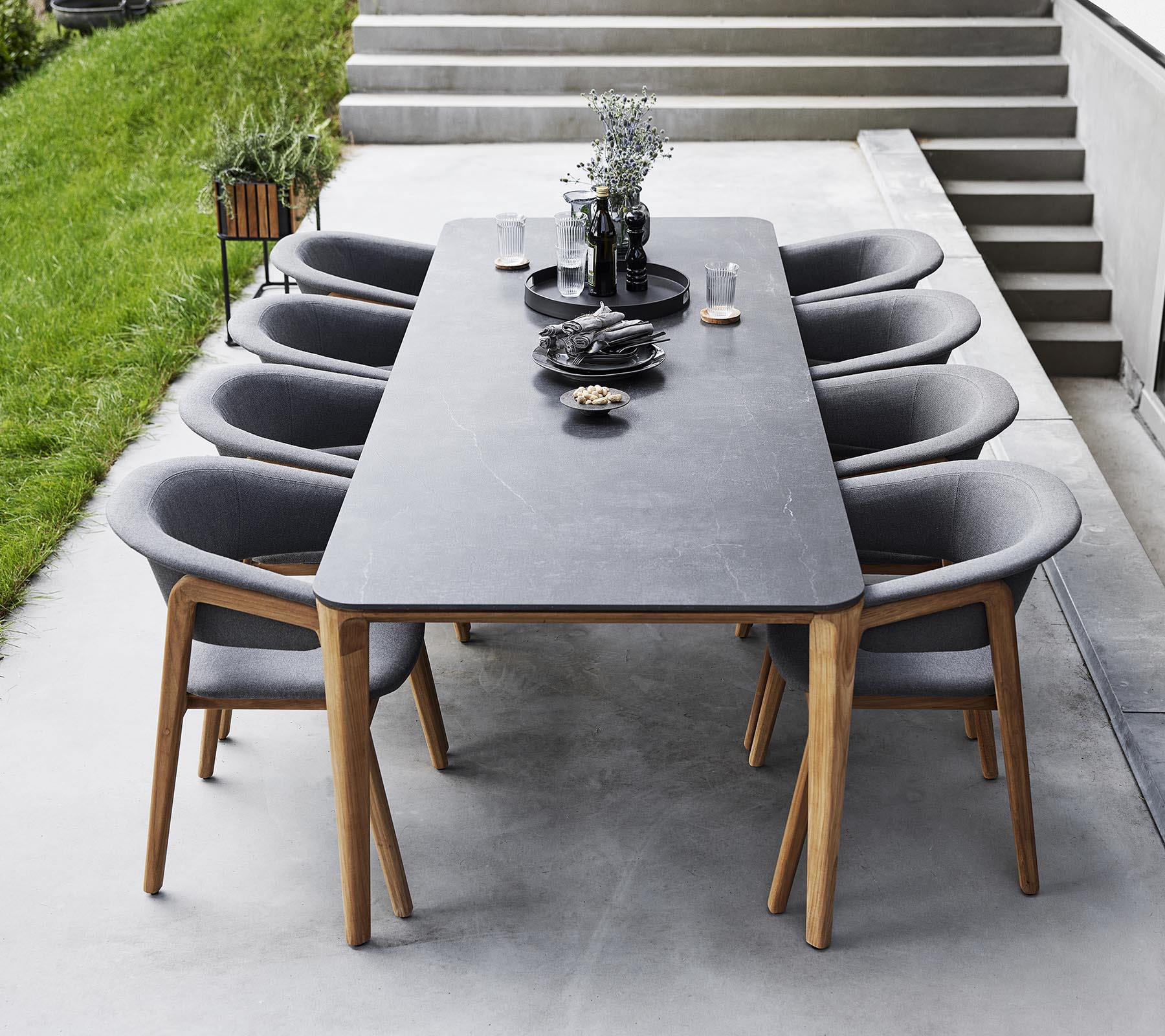 Installation de salle à manger élégante avec une grande table entourée de chaises rembourrées modernes, ornée d'objets décoratifs et de verdure.