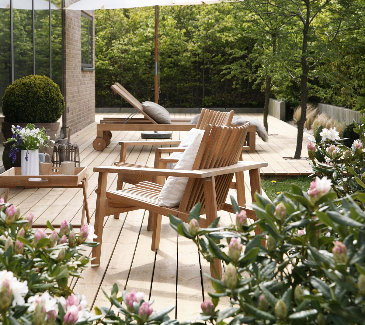 Des chaises en bois et une table sont entourées de verdure et de fleurs, créant un espace de détente extérieur serein et invitant.