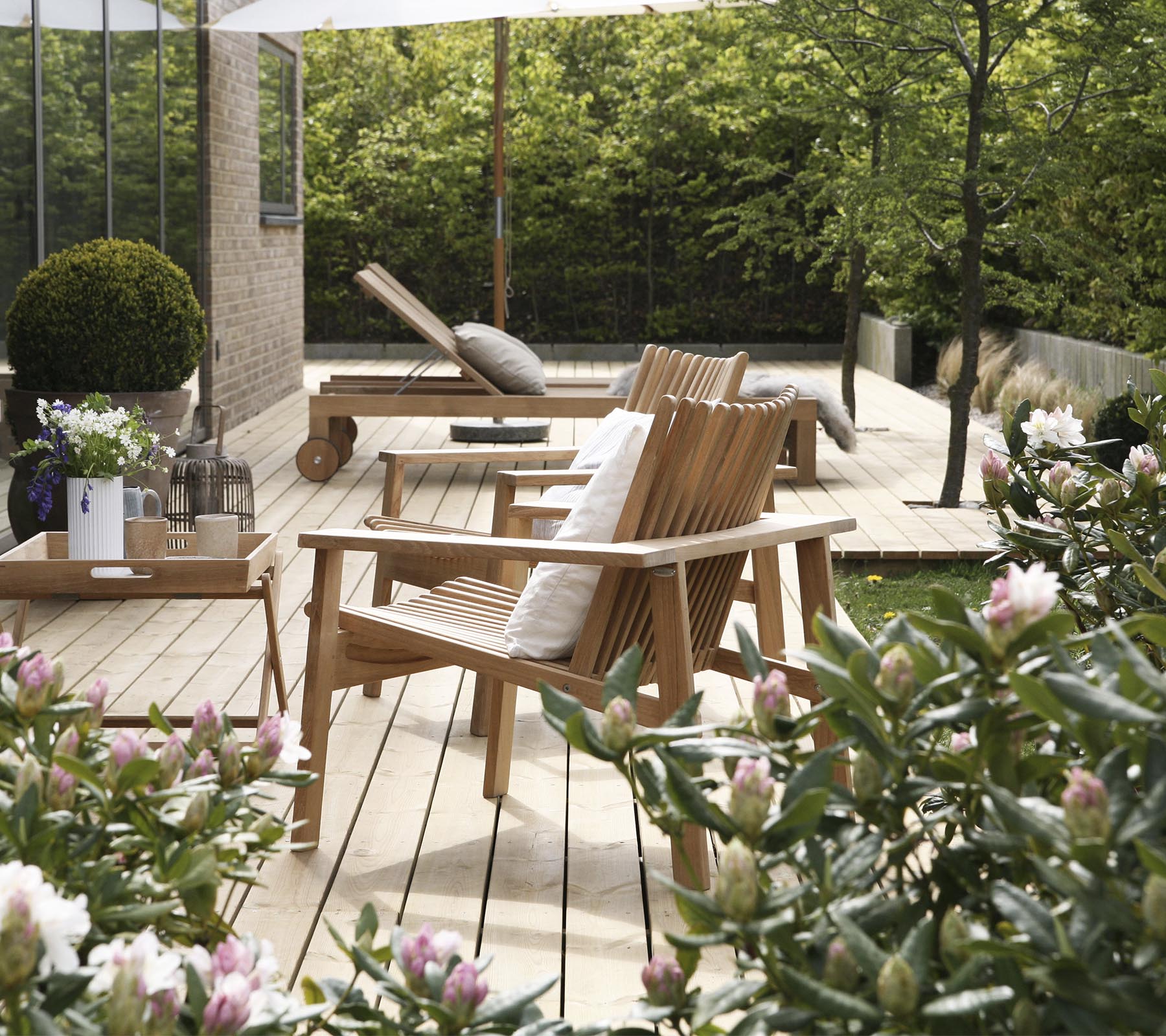 Des chaises en bois et une table sont entourées de verdure et de fleurs, créant un espace de détente extérieur serein et invitant.