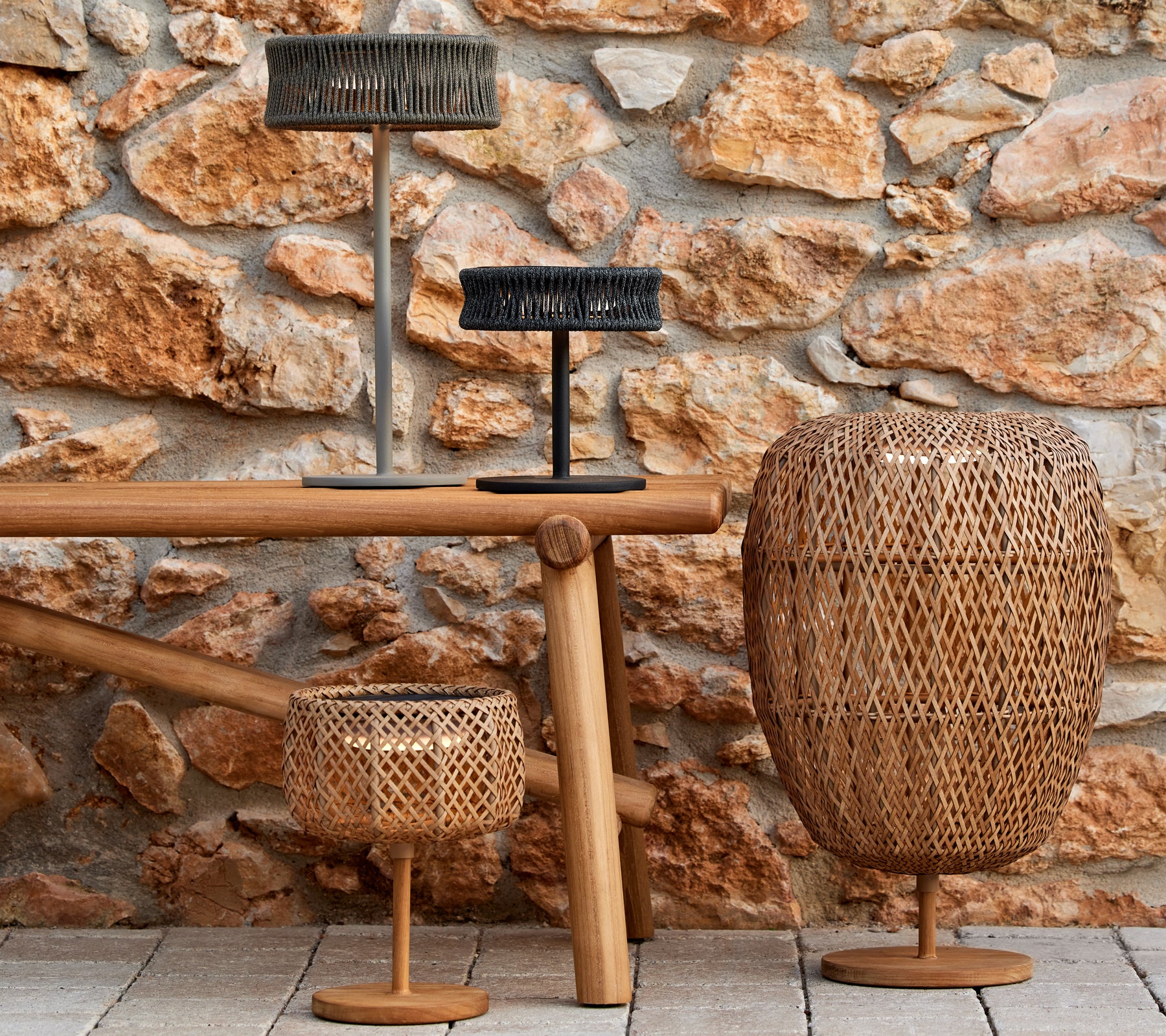 Trois lampes décoratives de différentes formes et tailles sur une table en bois, contre un mur en pierre texturé.