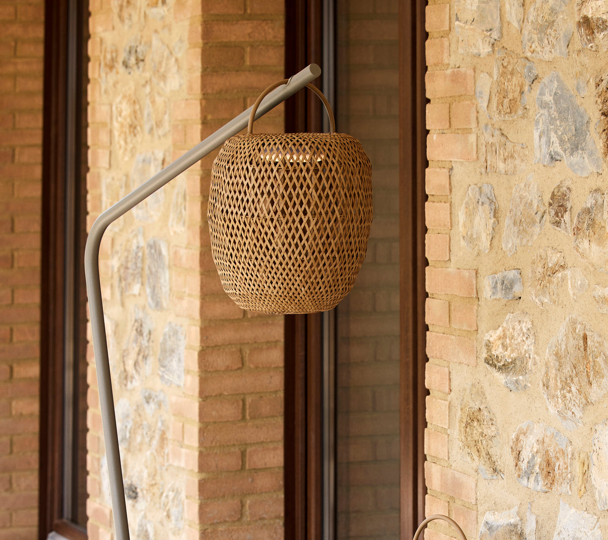 Une lampe tissée et luminescente suspendue à un support élégant, complétant un mur en pierre texturé.