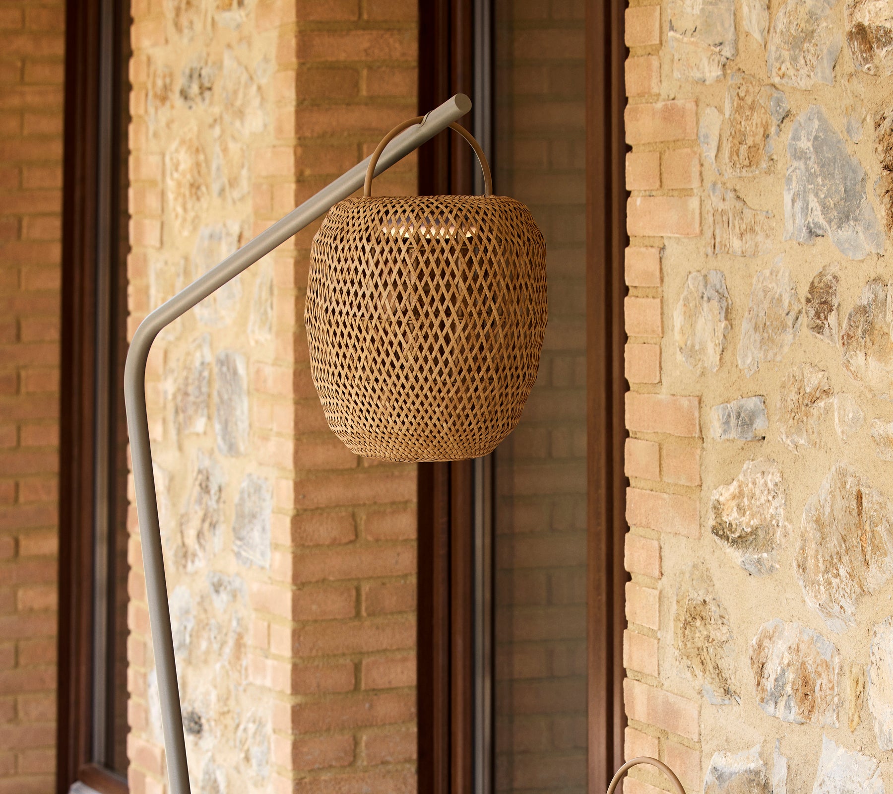 Une lampe tissée et luminescente suspendue à un support élégant, complétant un mur en pierre texturé.