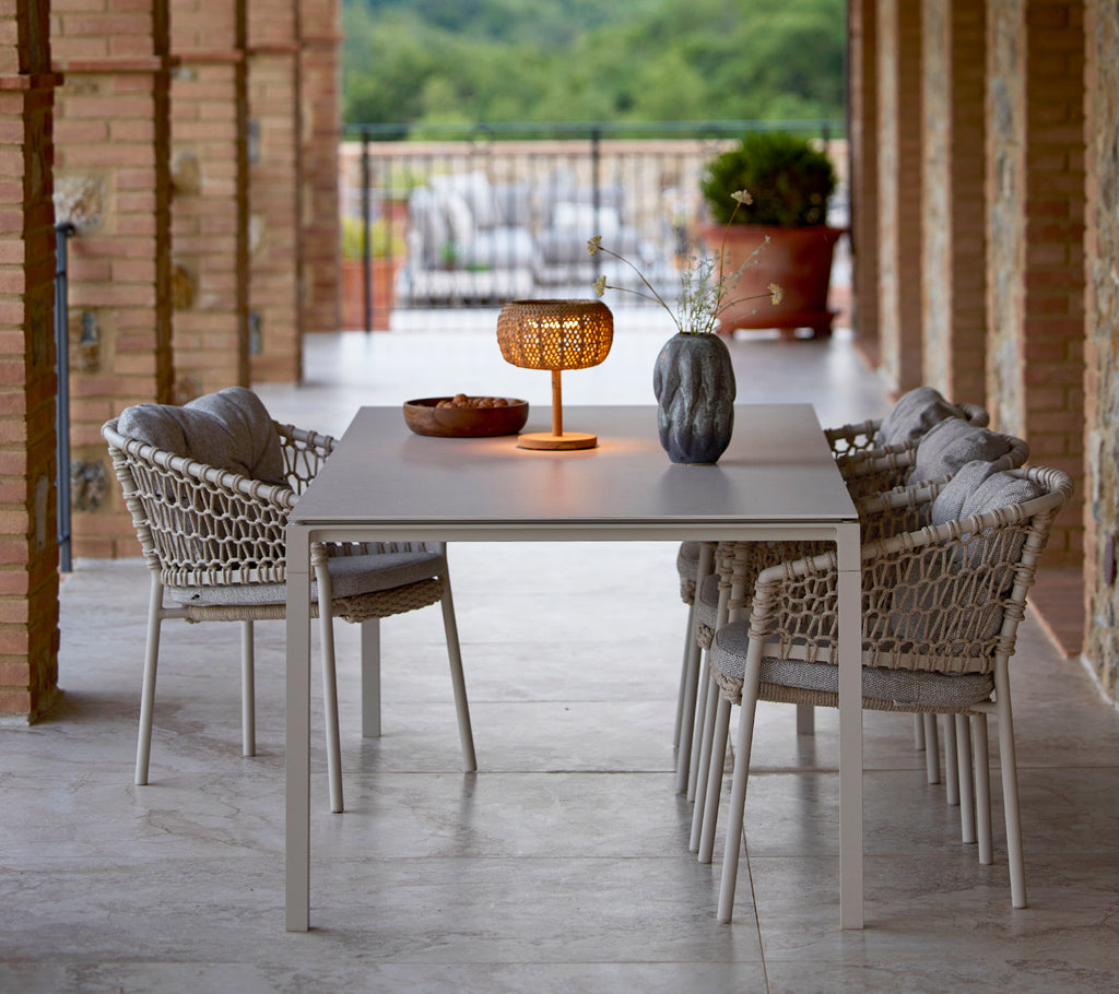 Une petite lampe de table lumineuse sur une table élégante, entourée de chaises de jardin stylées, créant une atmosphère chaleureuse et accueillante.