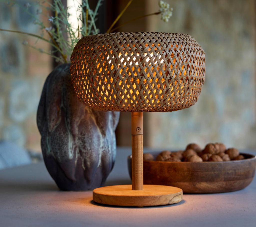 Petite lampe tissée avec une lueur chaude, complétée par un vase décoratif et un bol de noix, créant une atmosphère chaleureuse.