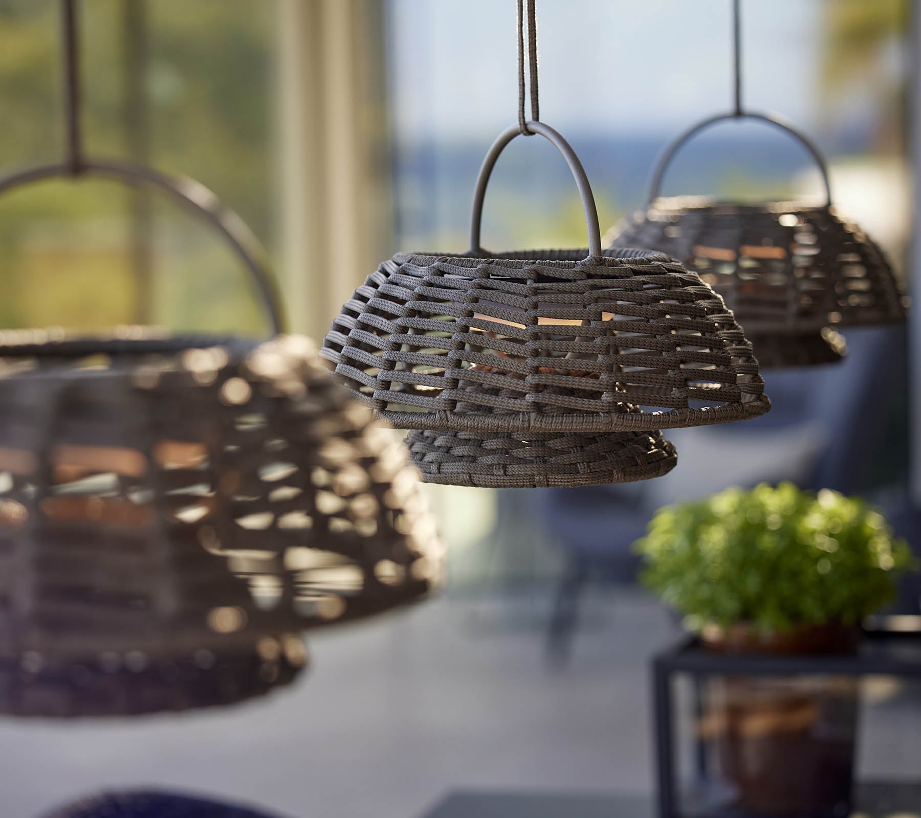Trois lampes tissées suspendues en rangée, créant une atmosphère chaleureuse et accueillante, complétée par une petite plante en pot.