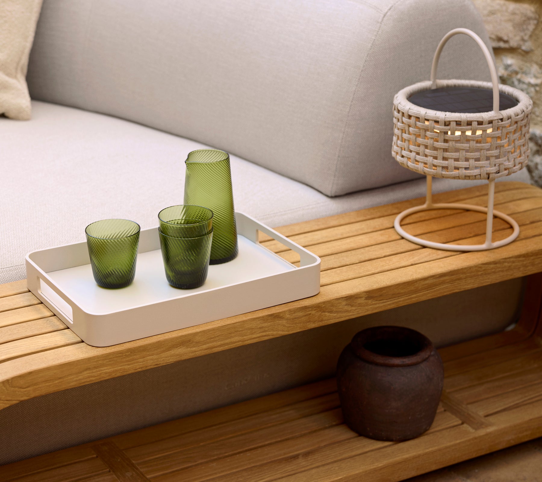 Une table basse confortable avec un plateau blanc, trois verres verts, une lampe tissée et un pot décoratif, qui renforce une ambiance sereine.