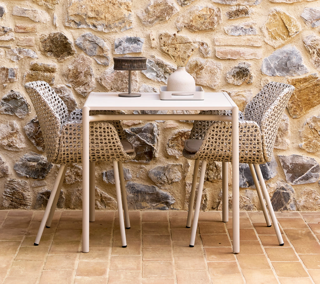 Une petite lampe d'illusion gris foncé sur une table Bliss avec deux chaises Vibe, entourée d'un mur en pierre texturé.