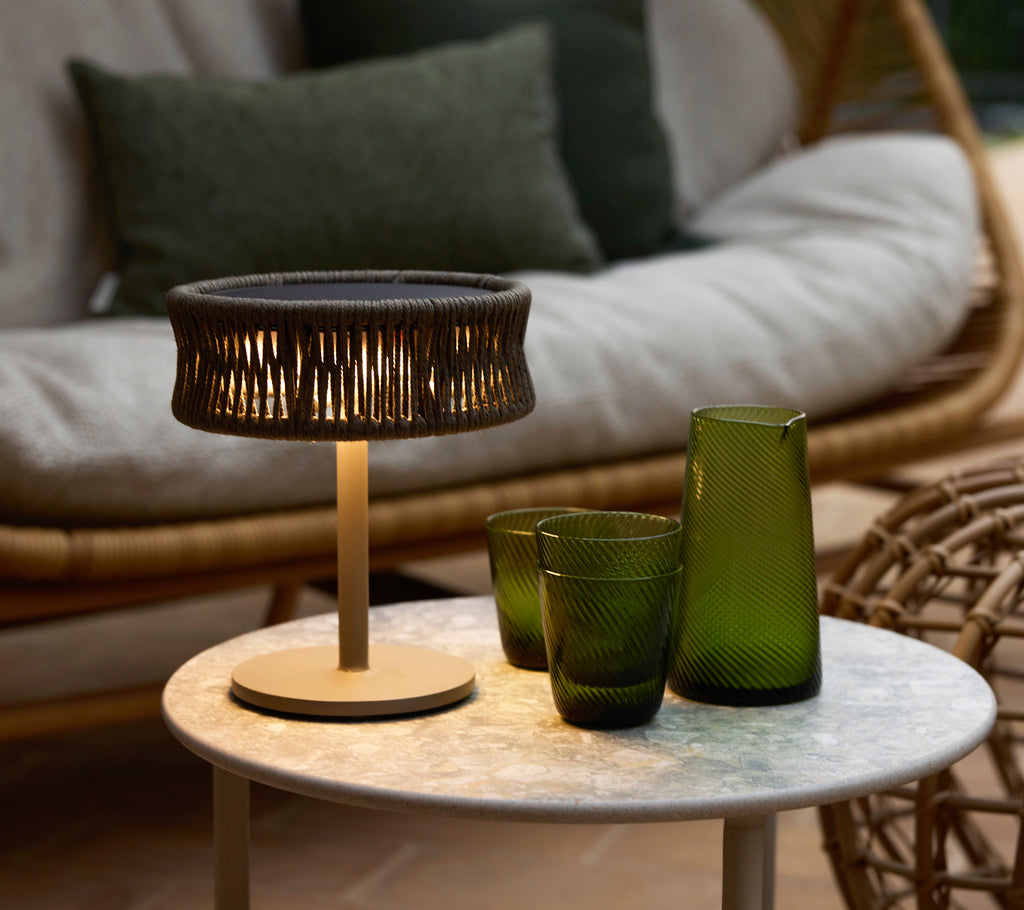 Une petite lampe à illusion gris foncé sur une table basse en marbre, accompagnée de vases en verre décoratifs verts et d'un coin salon douillet.