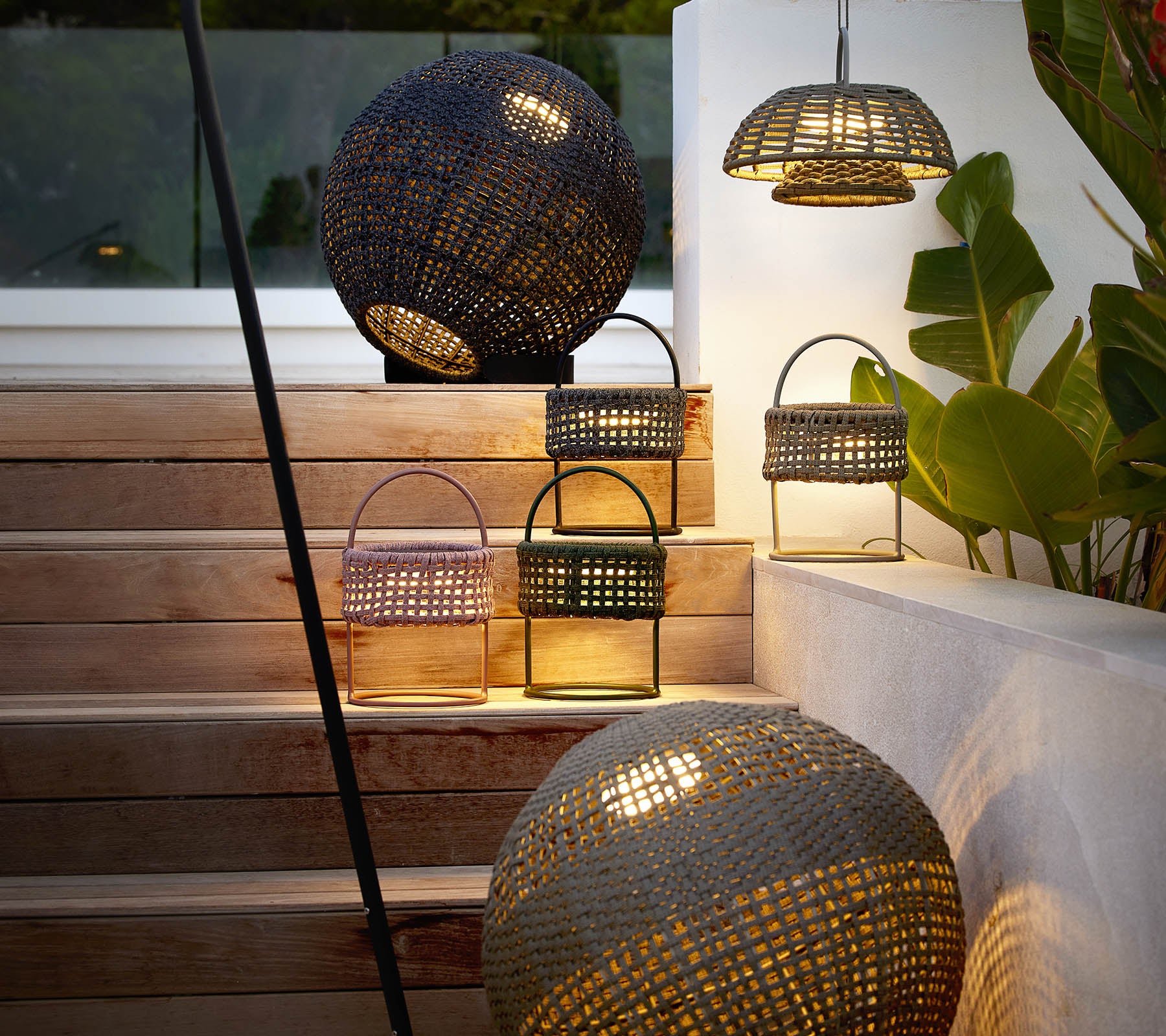 Une collection de lampes à illusions élégantes dans différentes formes, diffusant une lumière chaude et accueillante au milieu d'une verdure décorative.