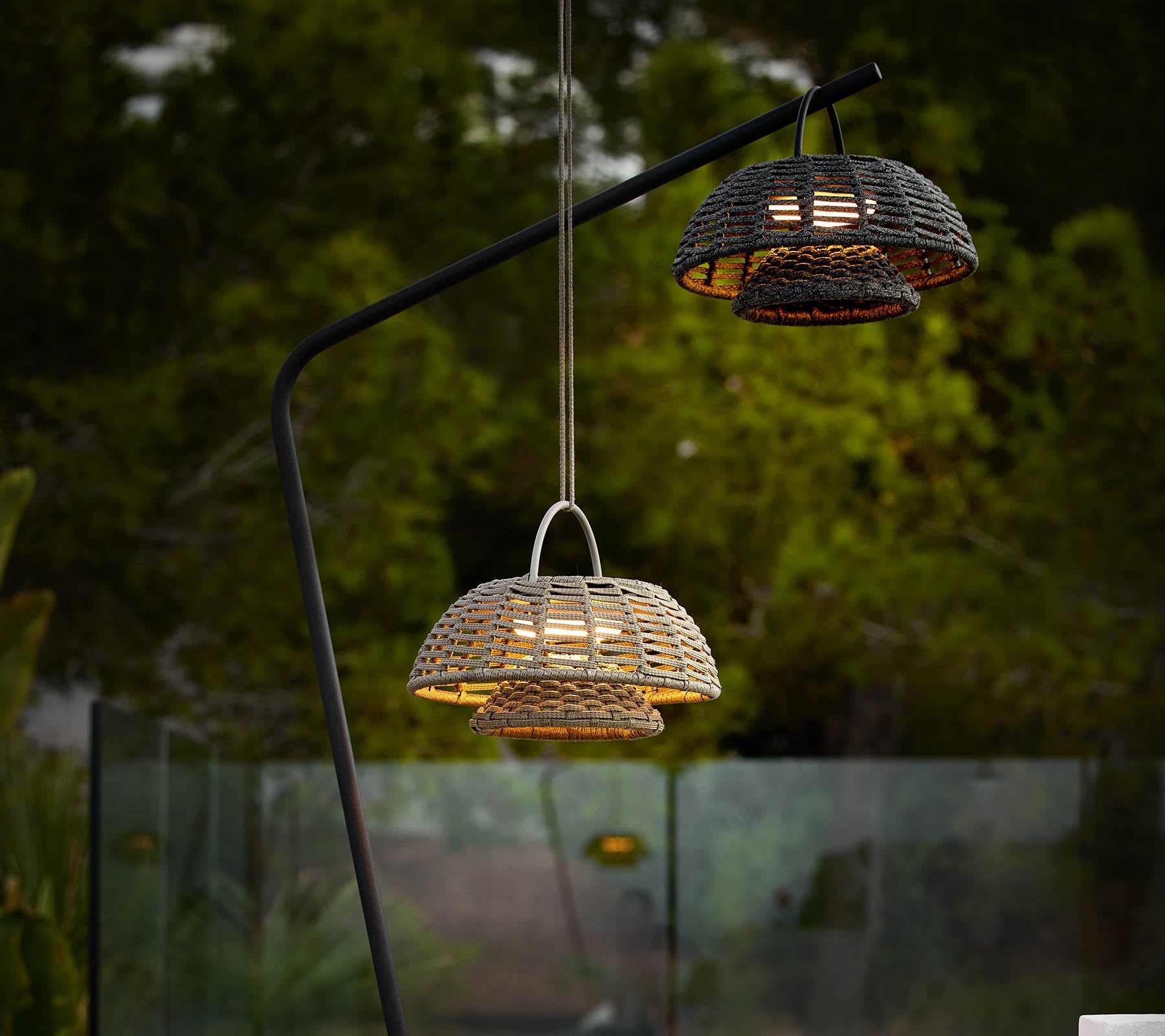 Deux lampes d'illusion avec des designs tissés, suspendues à un élégant support noir, projetant une lumière chaude sur un fond sombre.