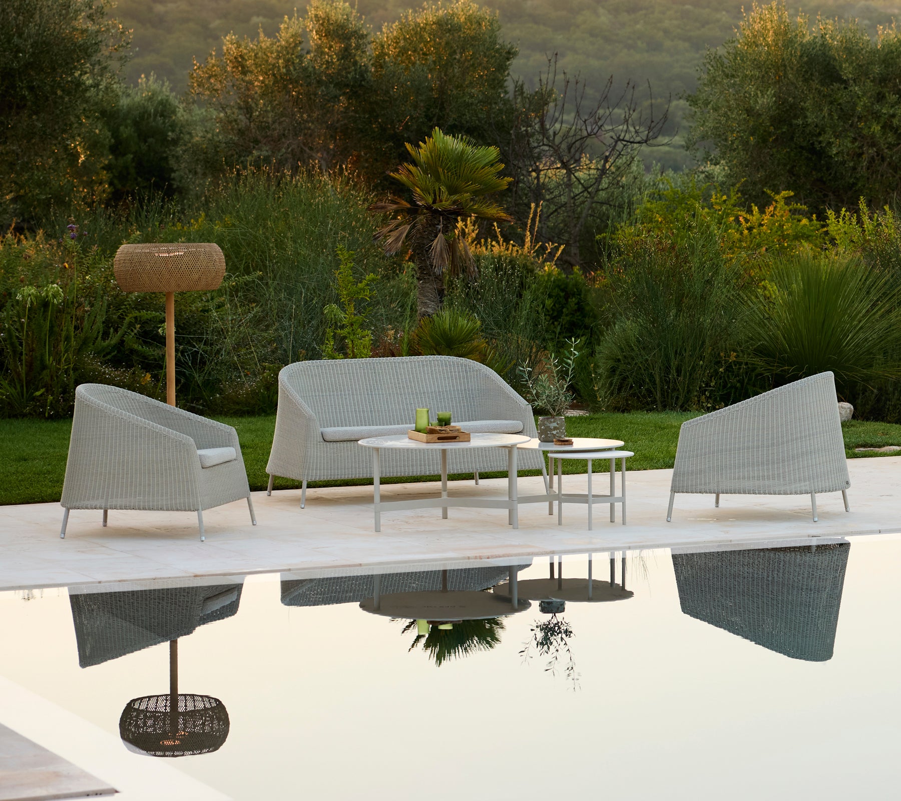 Canapé et fauteuil gris modernes avec une table blanche dans un cadre de lounge extérieur.