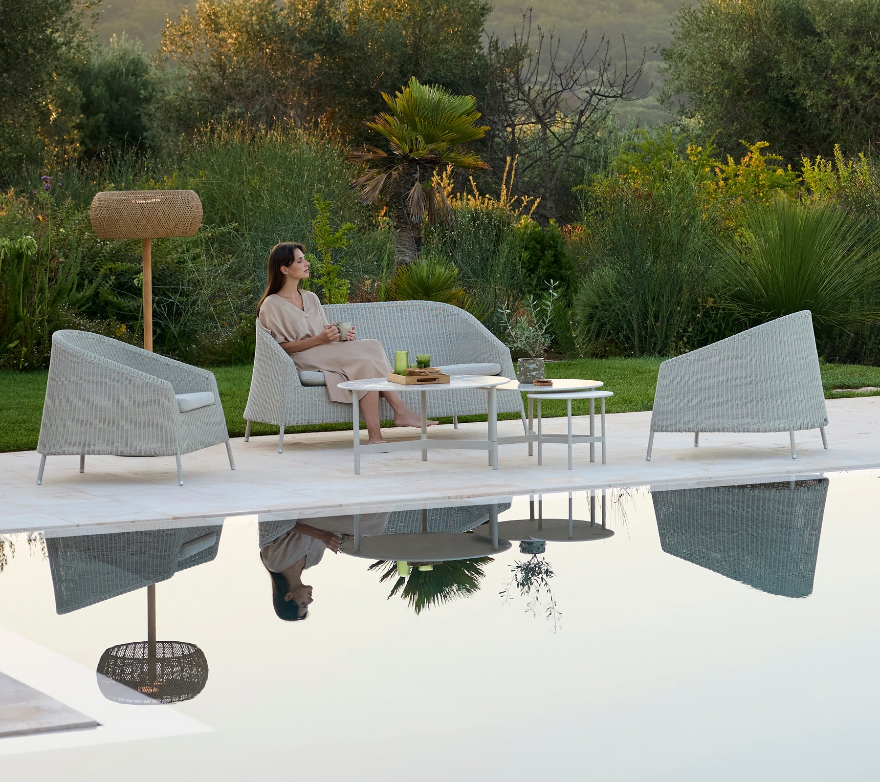 Canapé gris moderne et fauteuils autour d'une table blanche dans un salon extérieur relaxant.