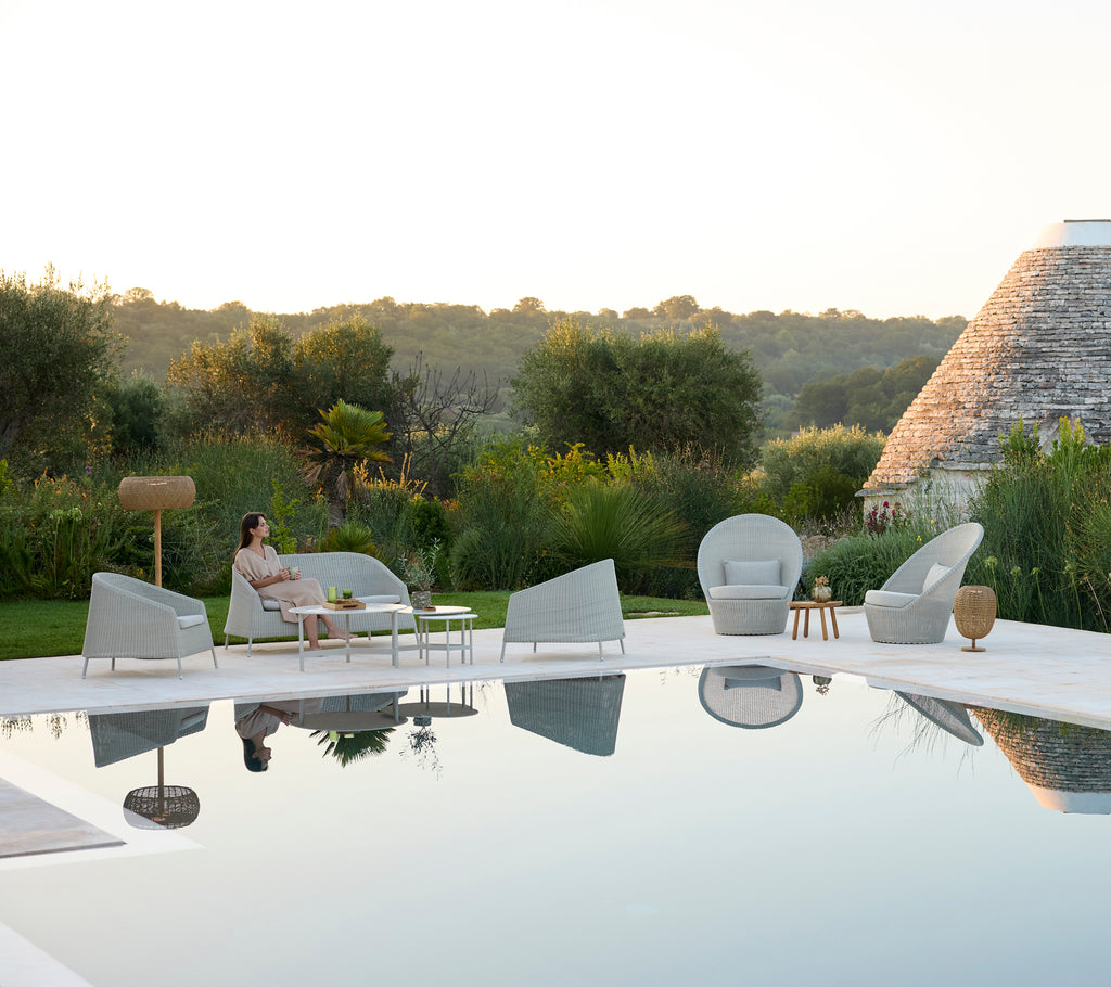 Espace lounge moderne en plein air avec des chaises grises et une table blanche près d'une piscine.