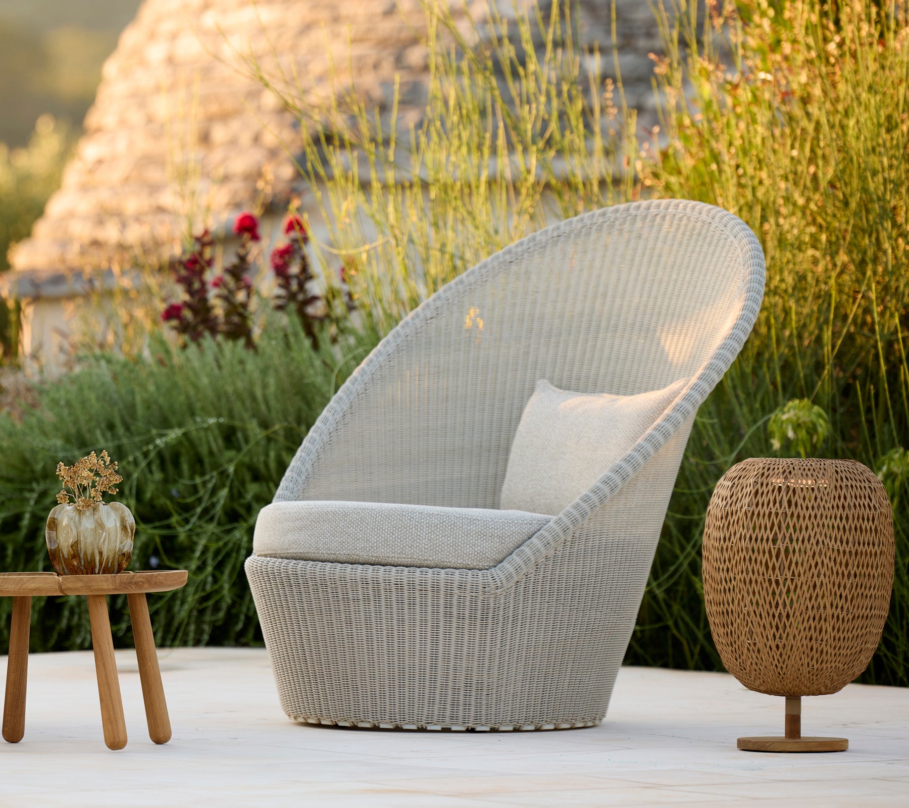 Chaise moderne grise avec coussin et table brune dans un cadre naturel en plein air.