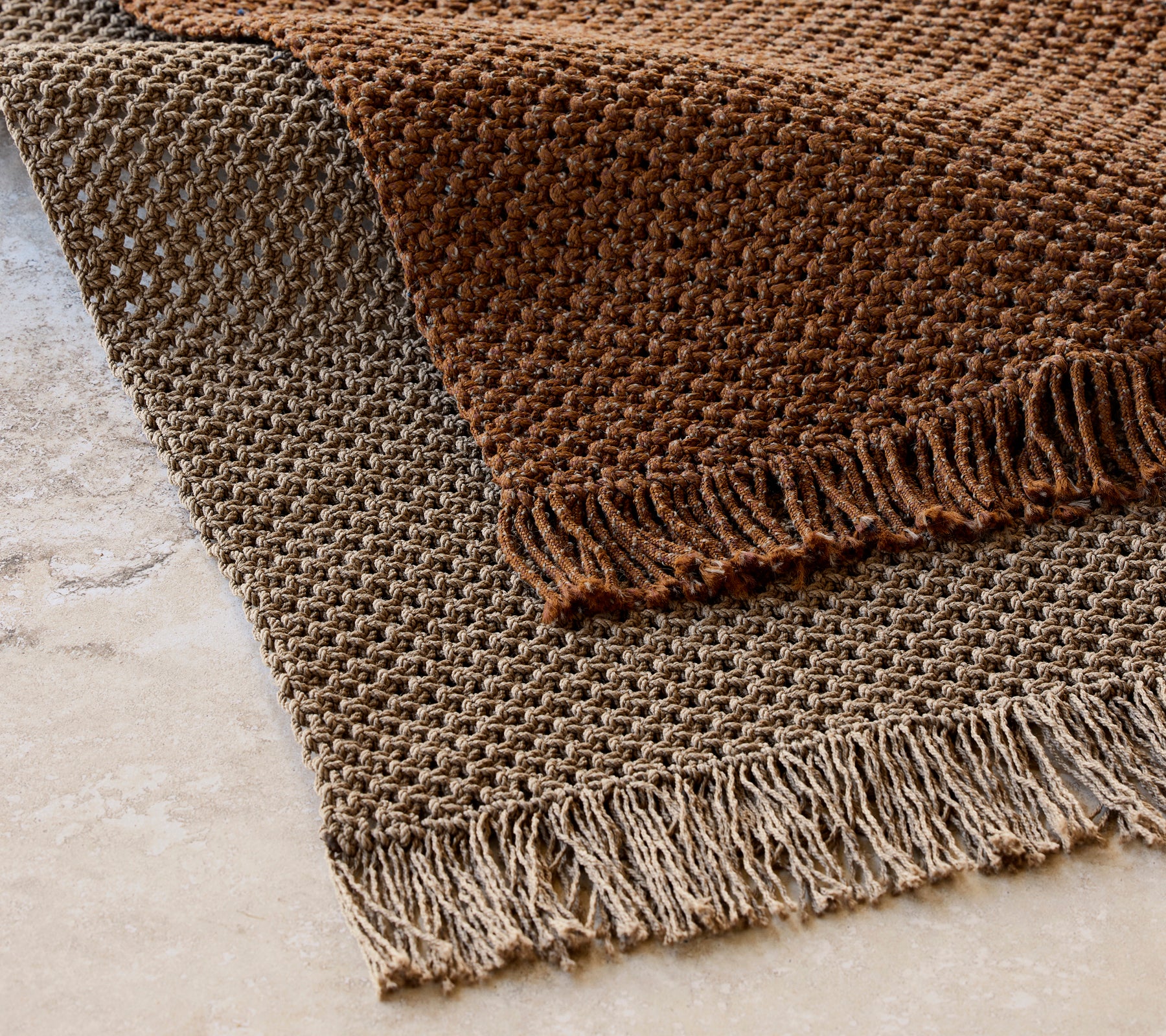 Tapis tricoté mesurant 240x170 cm dans un motif texturé avec des franges, présentant des tons bruns chauds.