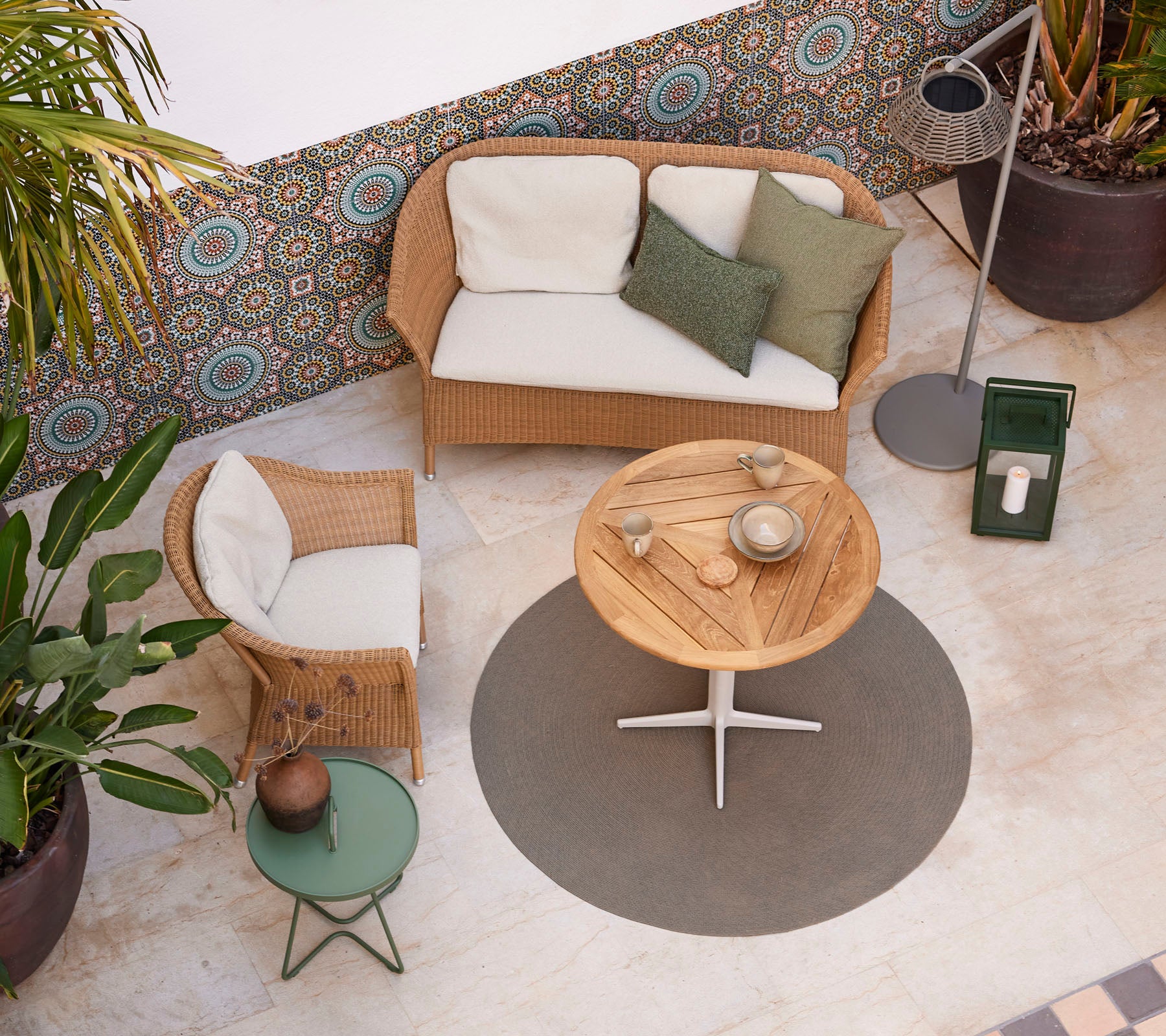 Un aménagement cosy avec un canapé en rotin, une table basse en bois ronde et des plantes en pot, améliorant une atmosphère élégante.
